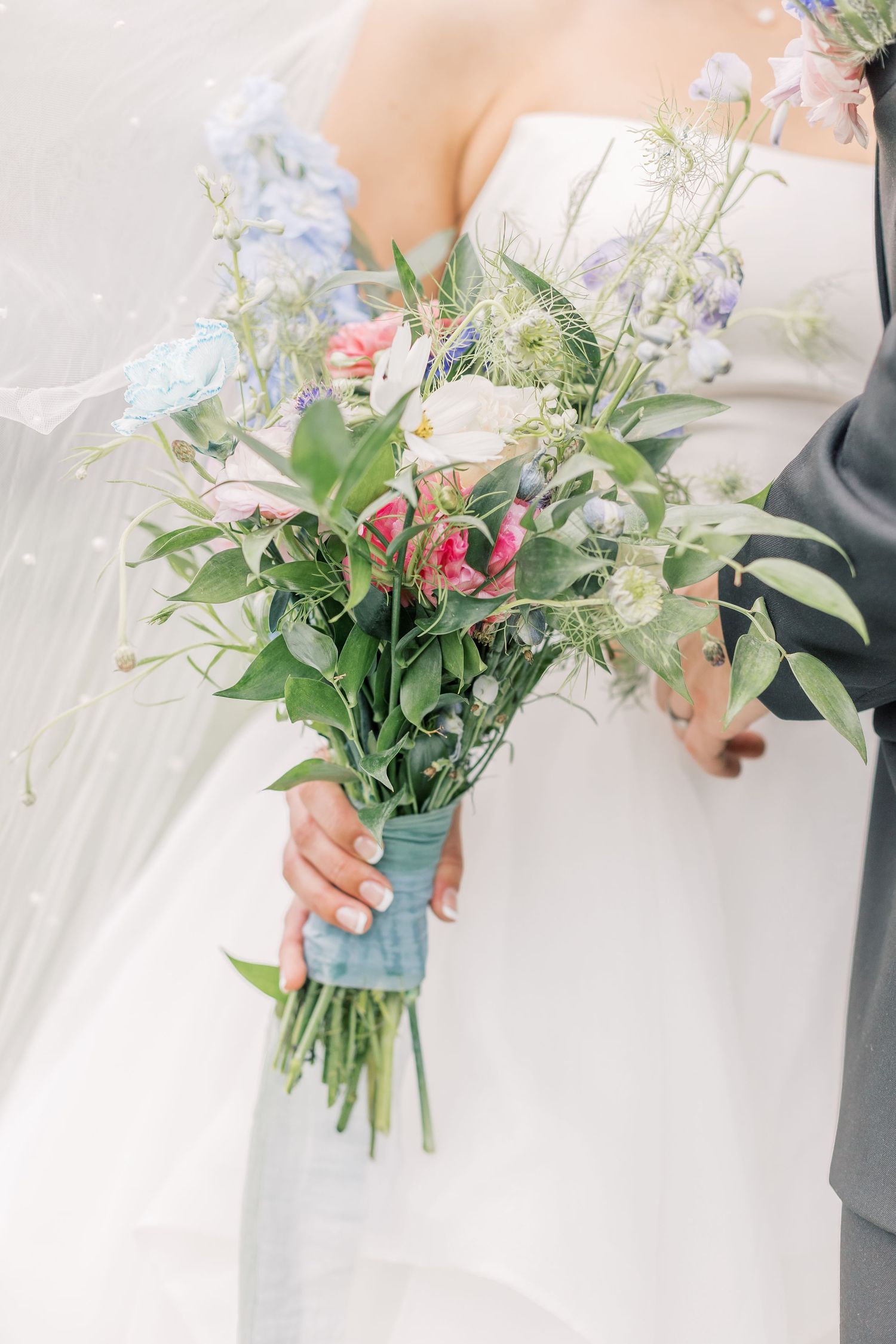 Close-up view of delicate pink and white floral wedding bouquet with greenery wrapped in blue ribbon.