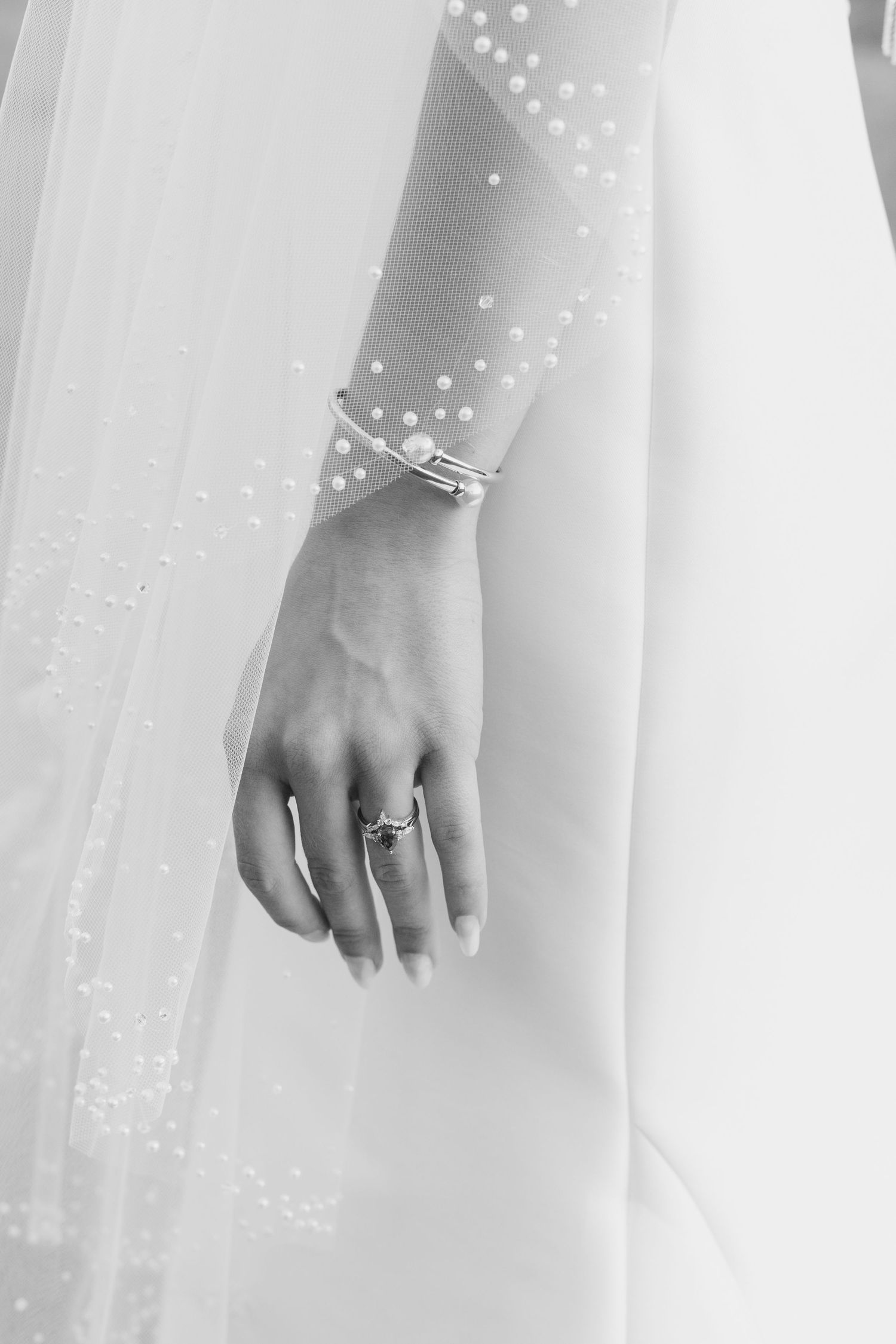 Close up view of a hand wearing an engagement ring against a white wedding dress background.