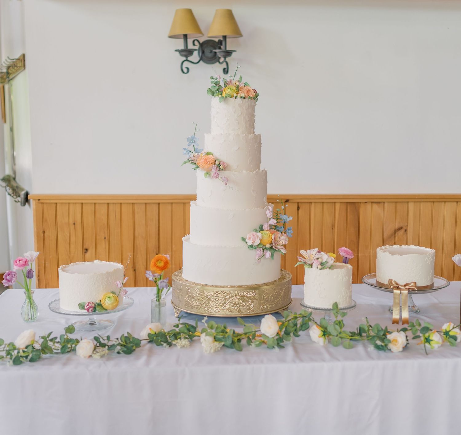 White wedding cake decorated with delicate pastel flowers and greenery displayed on an elegant table setting.
