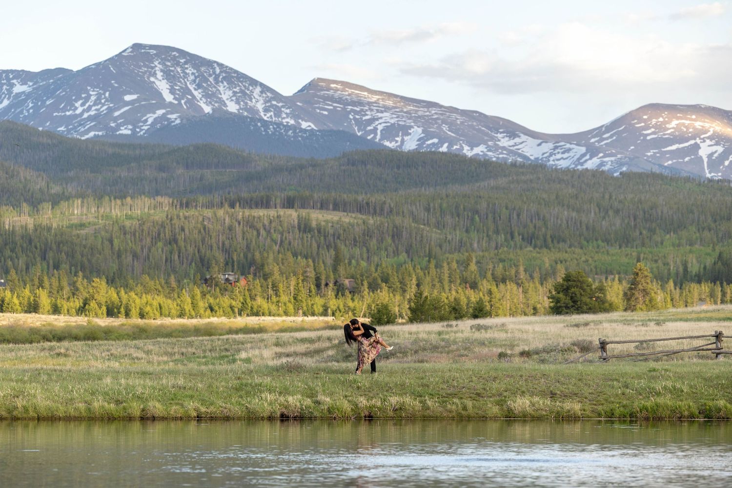 Couple dancing in a serene mountain meadow surrounded by lush forests and snow-capped peaks in the background.