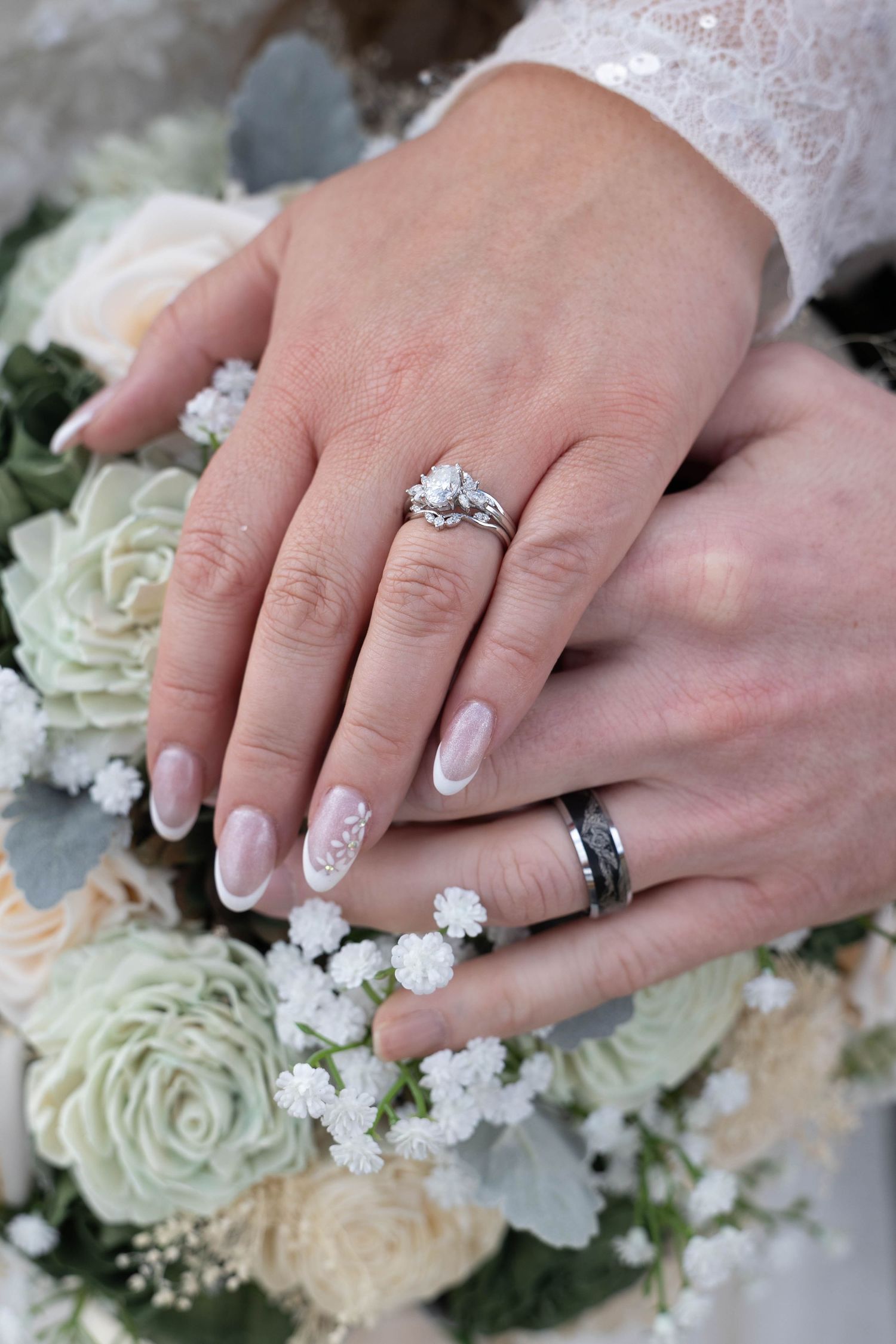 Newlyweds display wedding rings on bouquet of white roses, bride wearing diamond engagement ring and groom wearing black band.