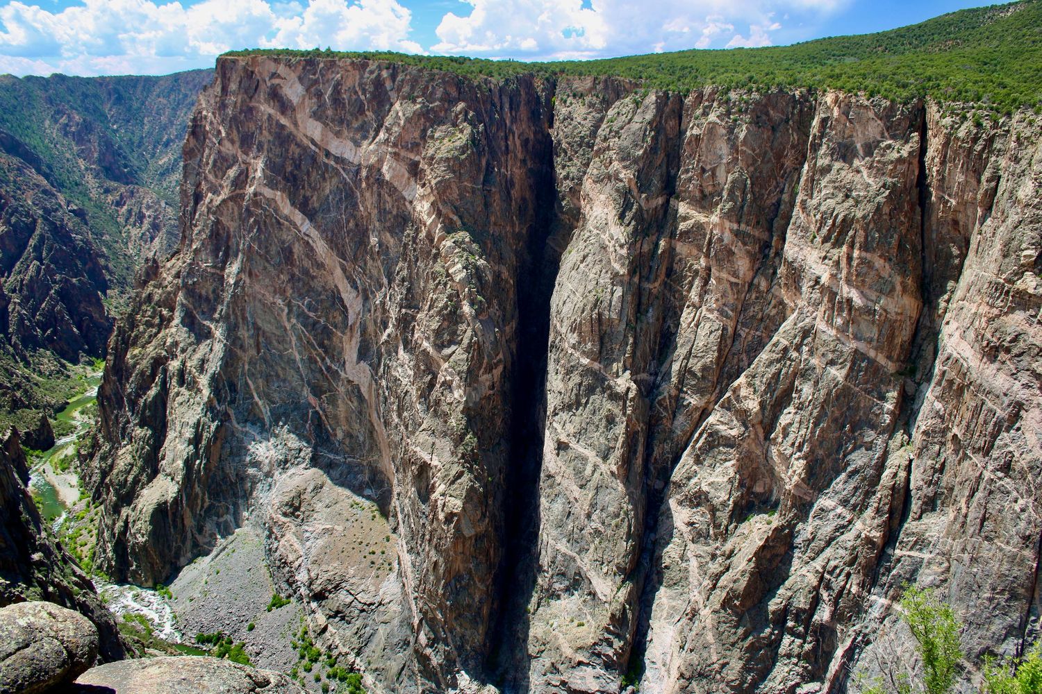 Panoramic view of Black Canyon of the Gunnison National Park showcasing steep cliffs and rugged terrain under blue skies.