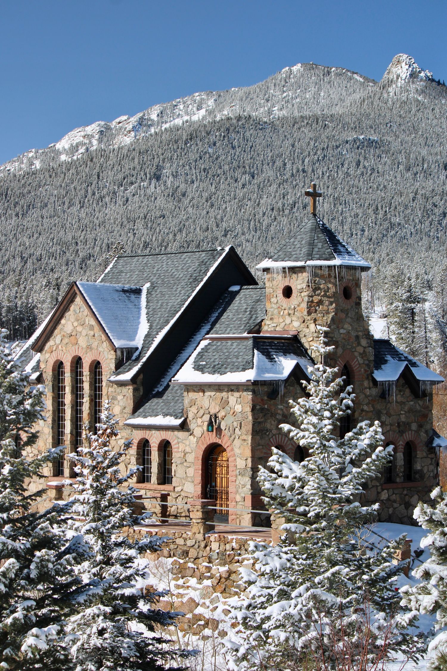 Historic stone chapel covered in snow with snow-capped Rocky Mountains in the background at Saint Malo near Estes Park.