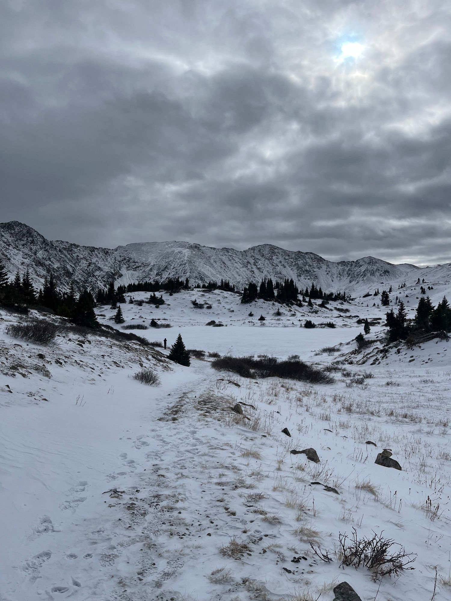 A panoramic winter landscape shows snow-covered mountains and slopes under dramatic cloudy skies in the Colorado Rockies. Loveland Pass.