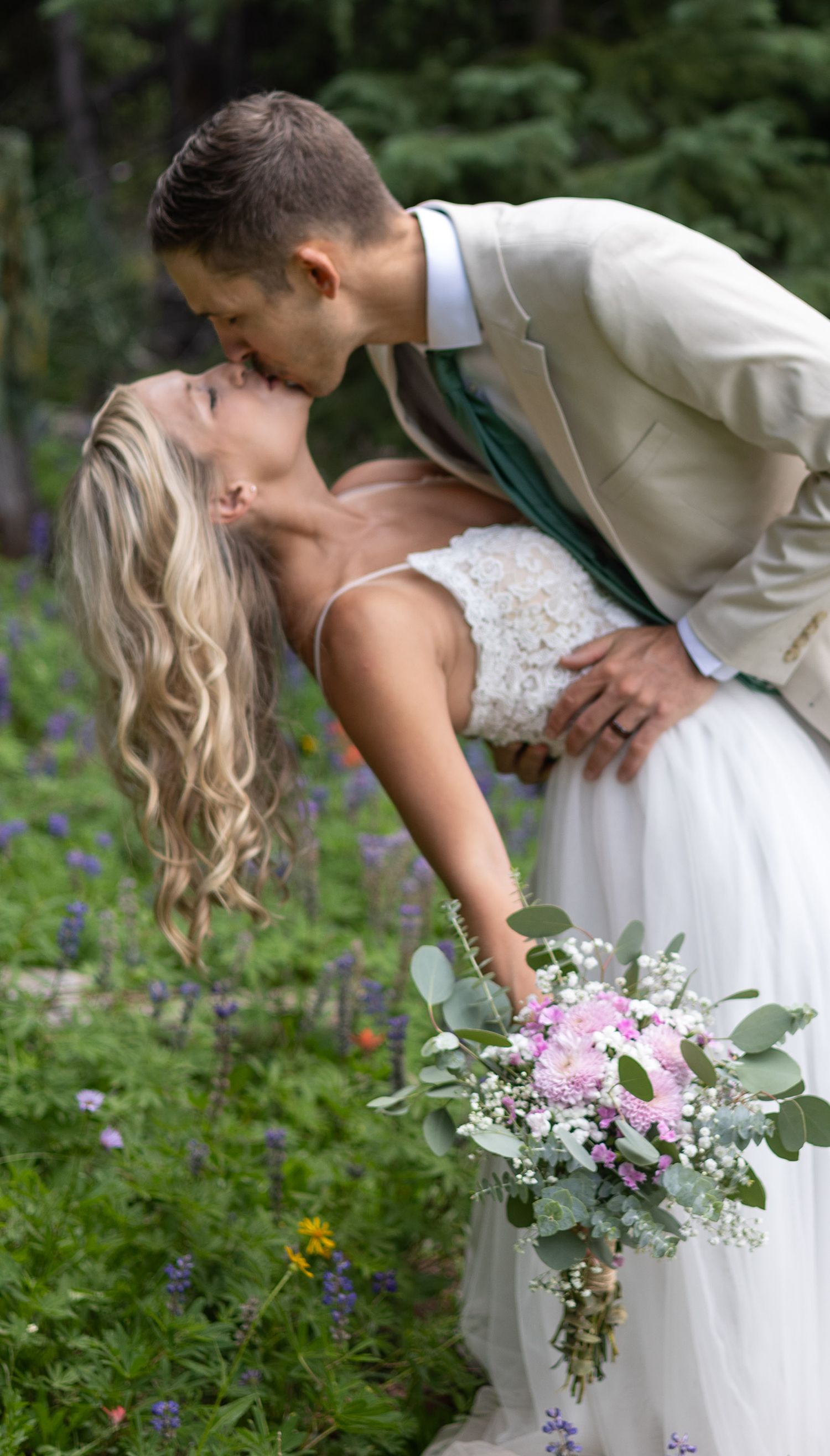 A romantic wedding couple shares a kiss in a garden while the bride holds a beautiful pink and white floral bouquet.