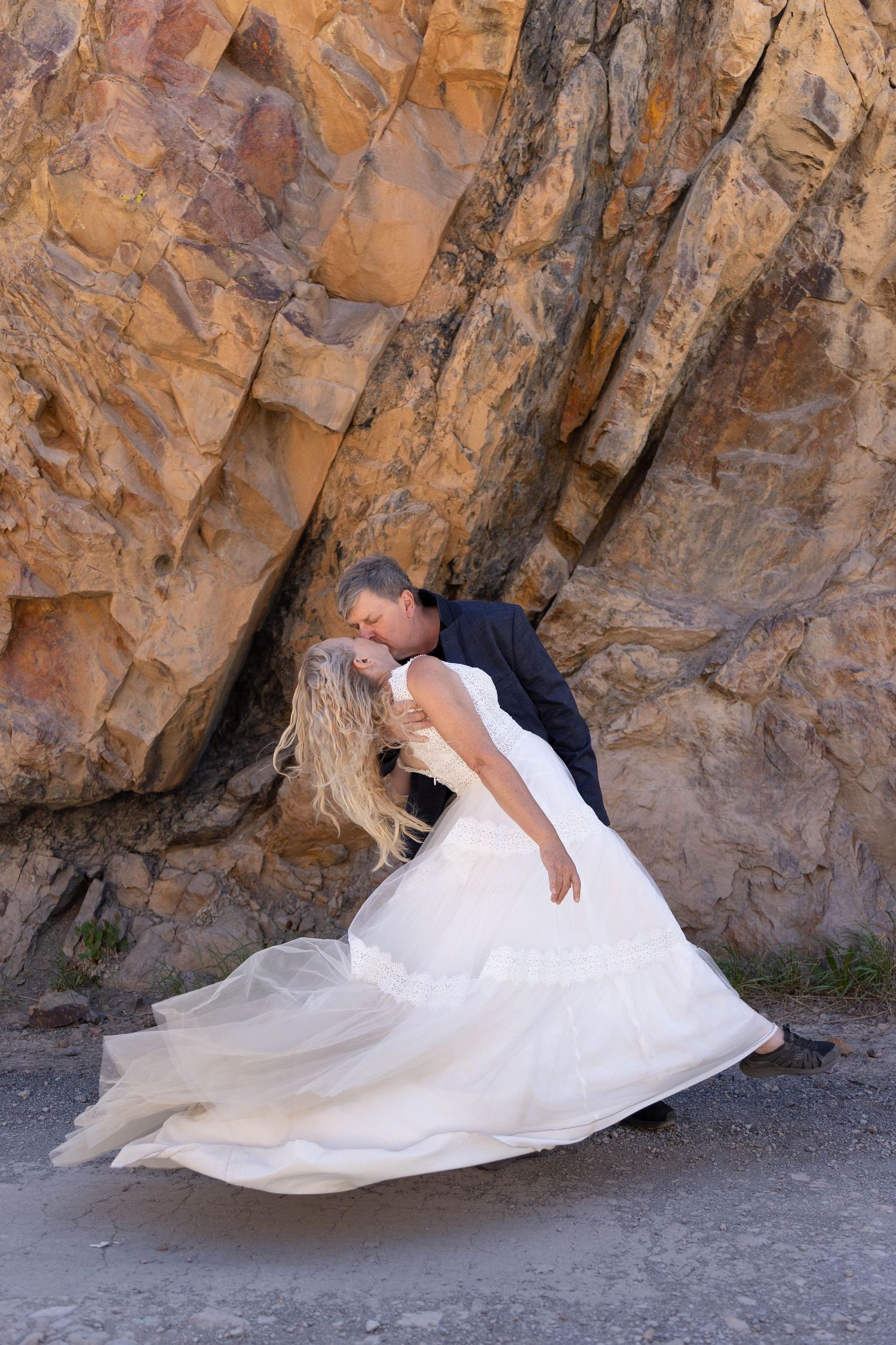 Bride and groom sharing a romantic dip kiss in front of dramatic golden rock formations outdoors.