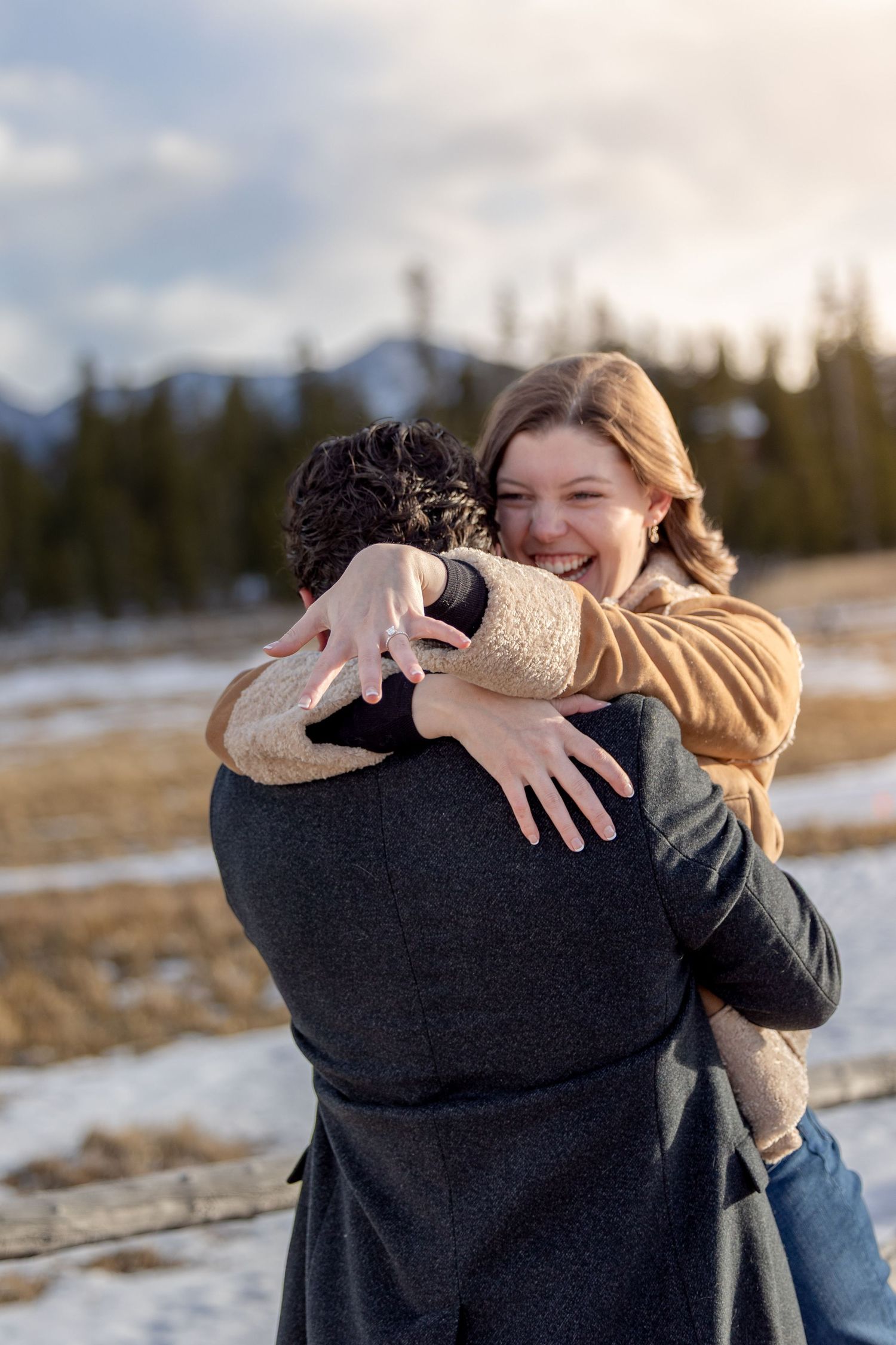 Happy woman smiling and hugging her partner outdoors in a snowy mountain landscape after a proposal.