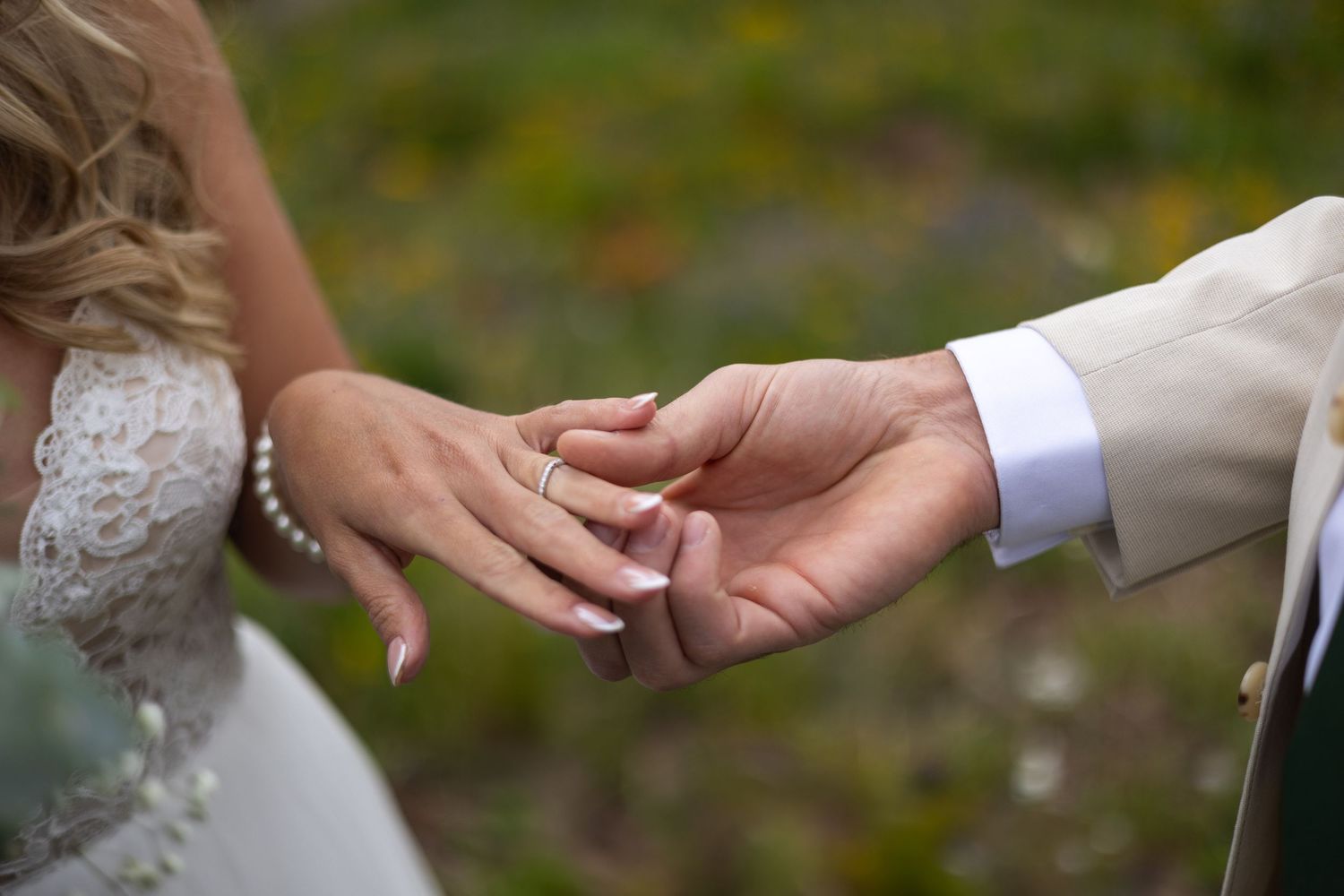 Close-up of hands exchanging wedding rings during an outdoor ceremony with a blurred natural background.