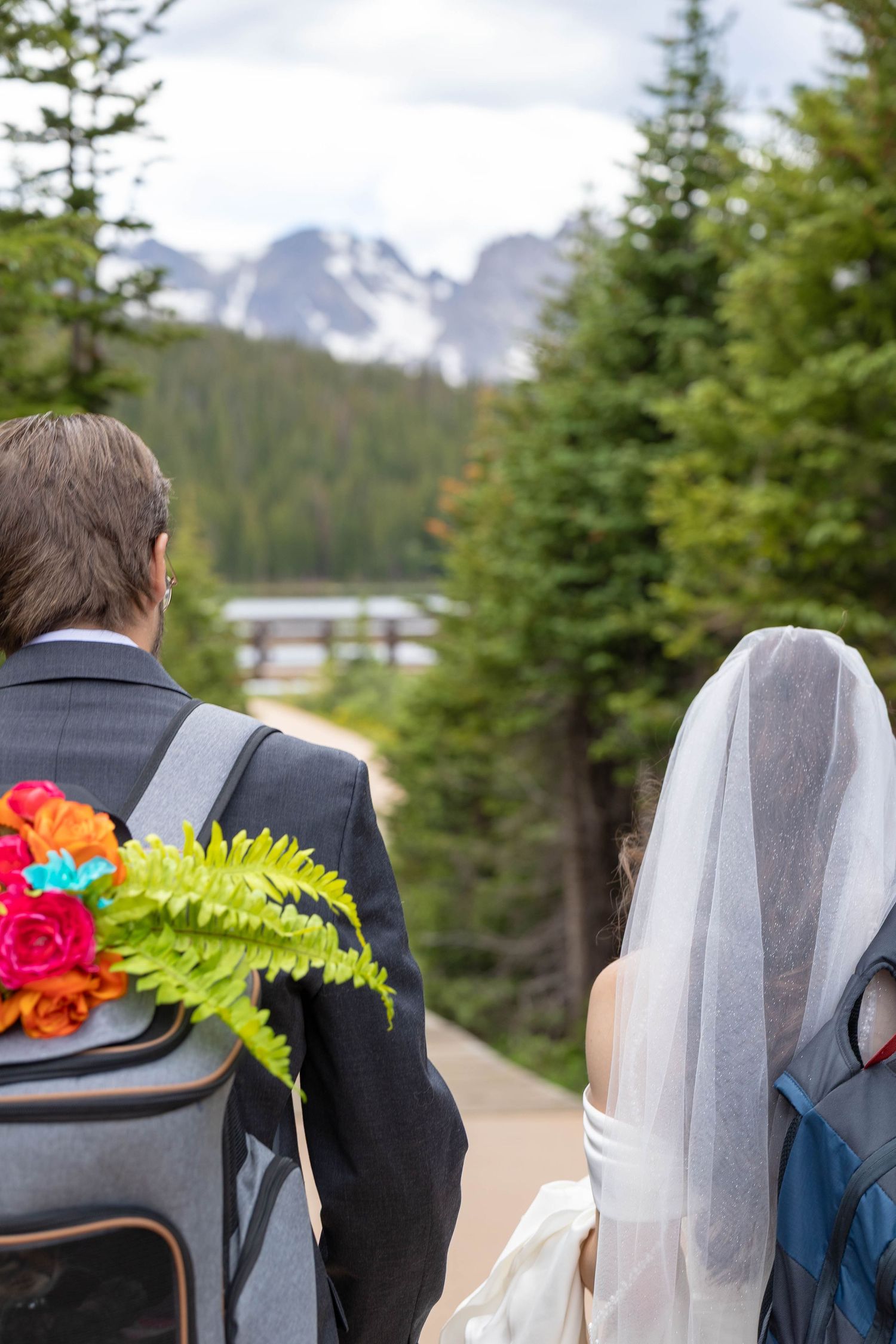 Bride and groom walking toward a mountain lake surrounded by pine trees on their wedding day.