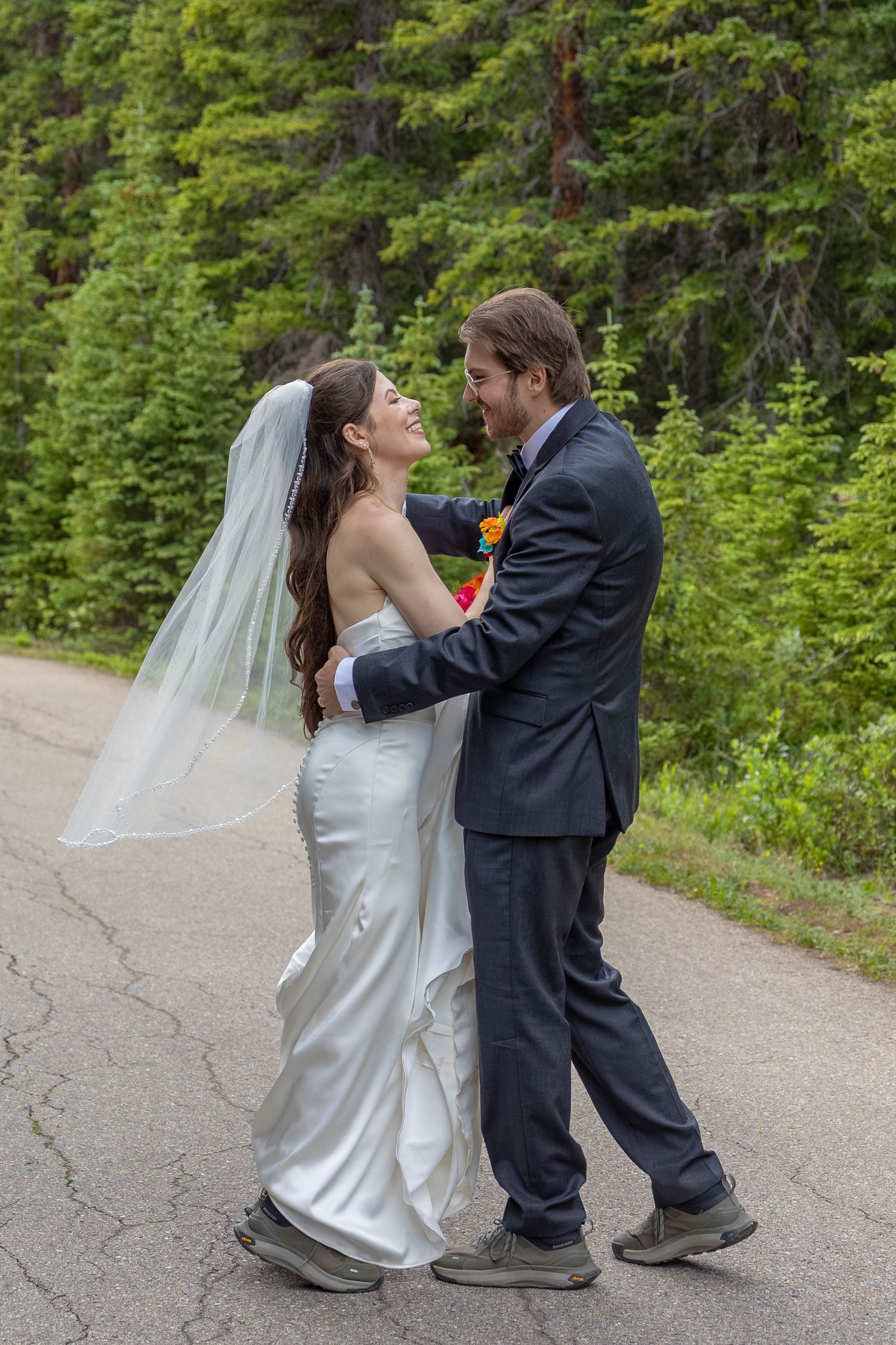 Happy bride and groom dancing on a road surrounded by lush green forest on their wedding day.