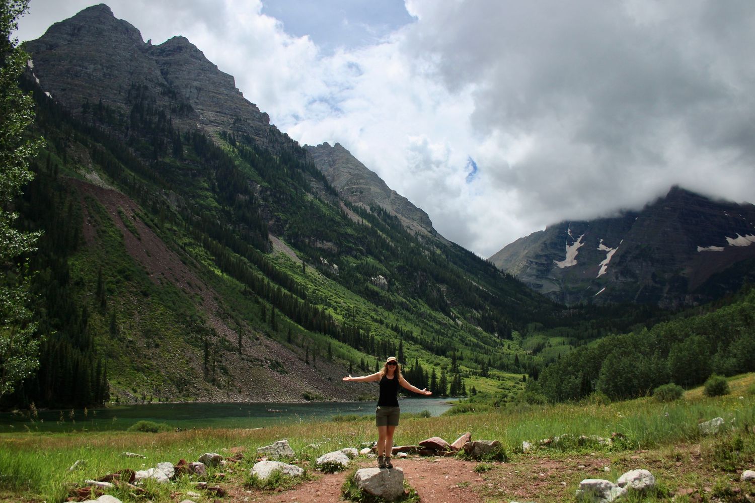 Woman standing on rock with arms outstretched before Maroon Bells peaks and alpine lake in Colorado.