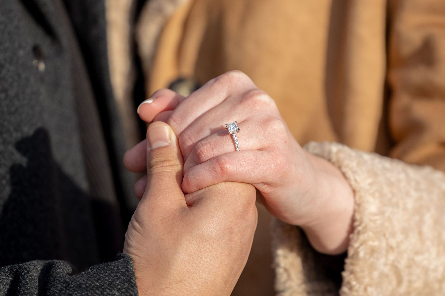 Close-up of couple holding hands with a sparkling diamond engagement ring on womans finger.