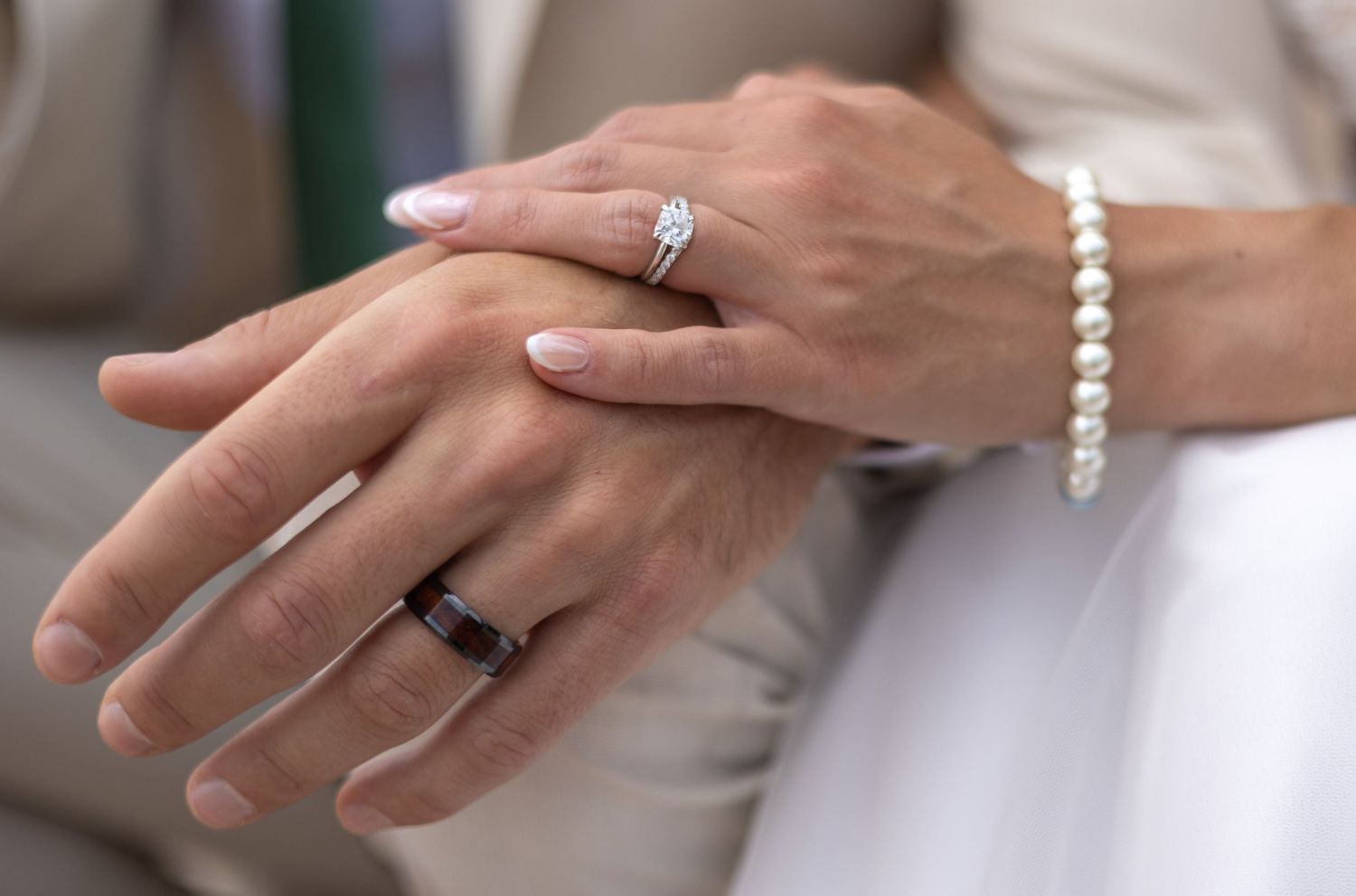 Close-up of hands wearing wedding rings and a pearl bracelet during a wedding ceremony.