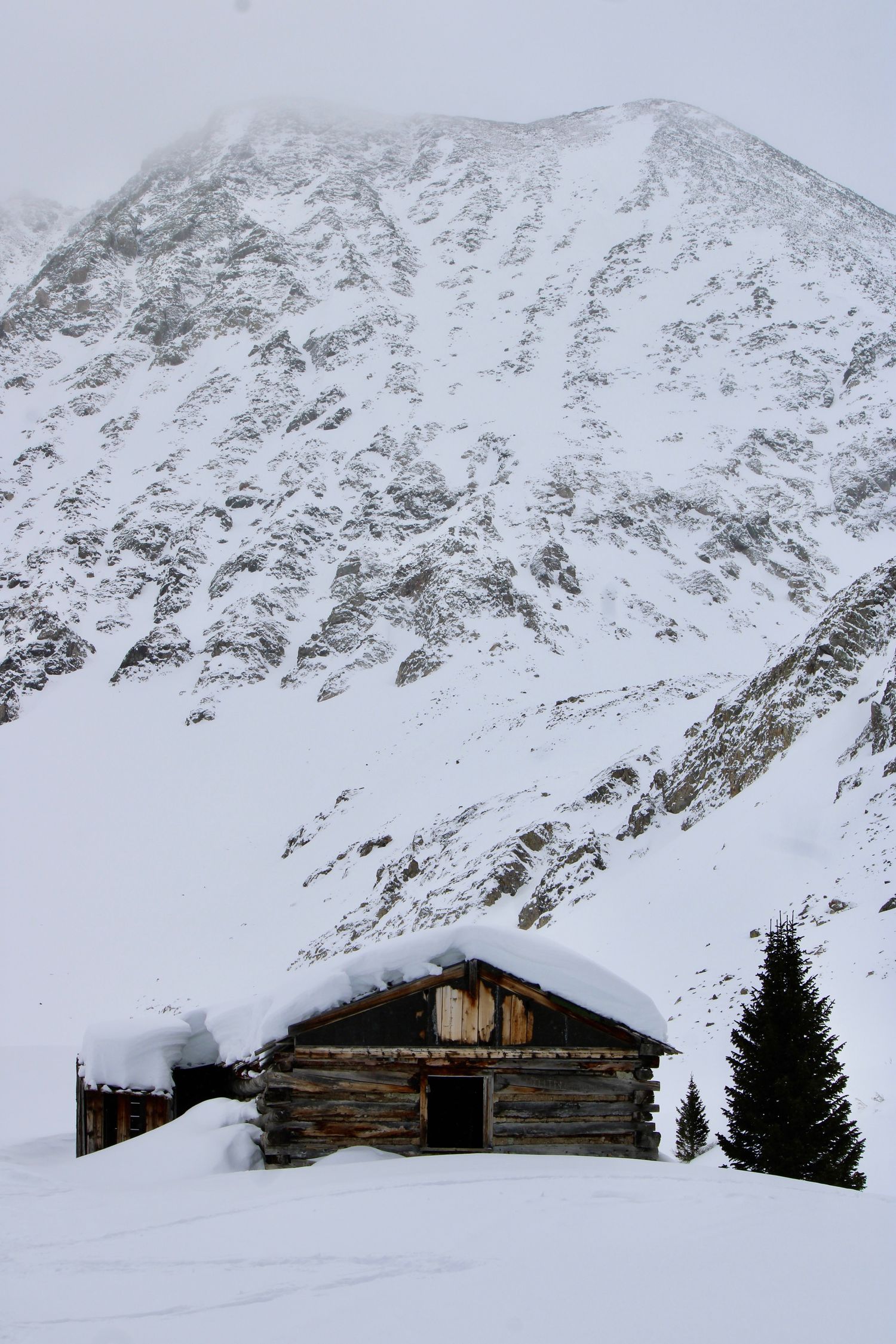 Snow-covered mountain landscape with rustic log cabins nestled at the base of steep winter slopes.