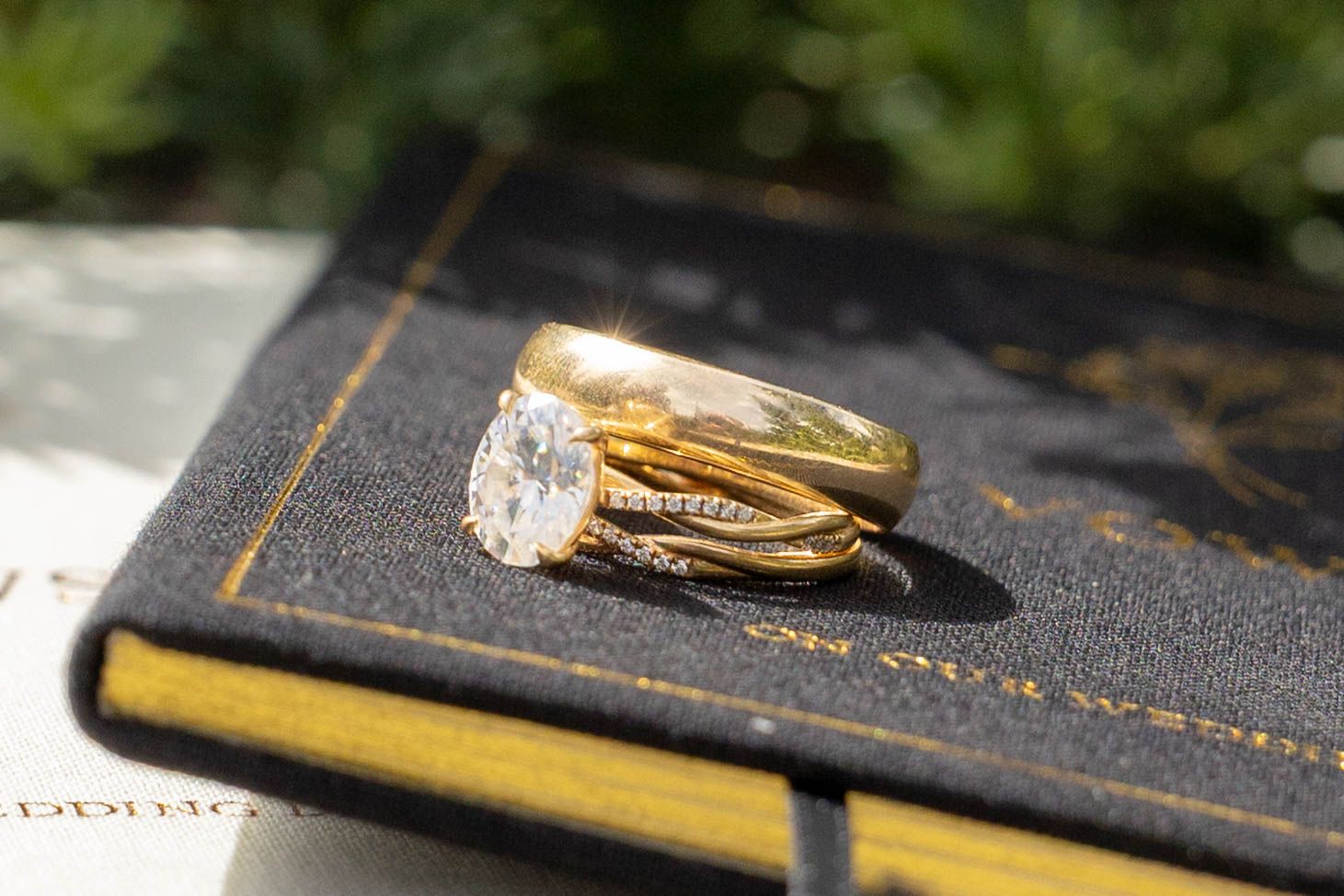 Gold engagement ring with oval diamond and wedding band set displayed on a dark book outdoors.