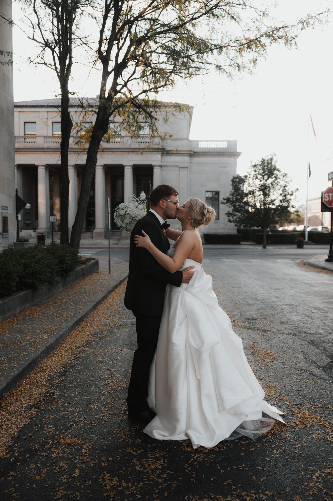 Romantic wedding photos of a couple dancing in front of a classical building at dusk.