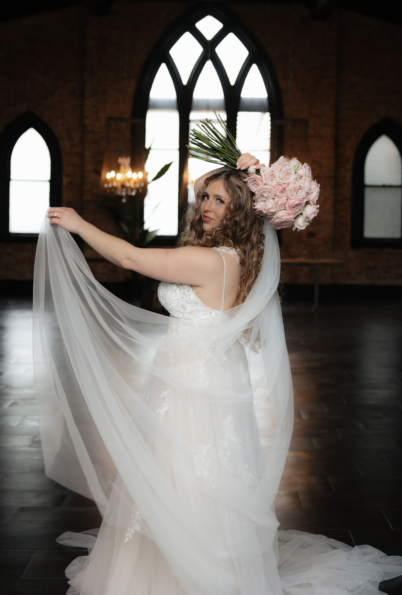 A bride in a flowing white dress twirls gracefully in a church with gothic windows.