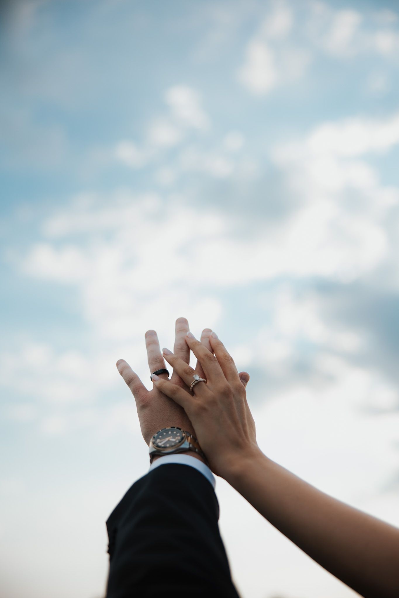 Close-up shots of hands with wedding rings against a blue cloudy sky background.