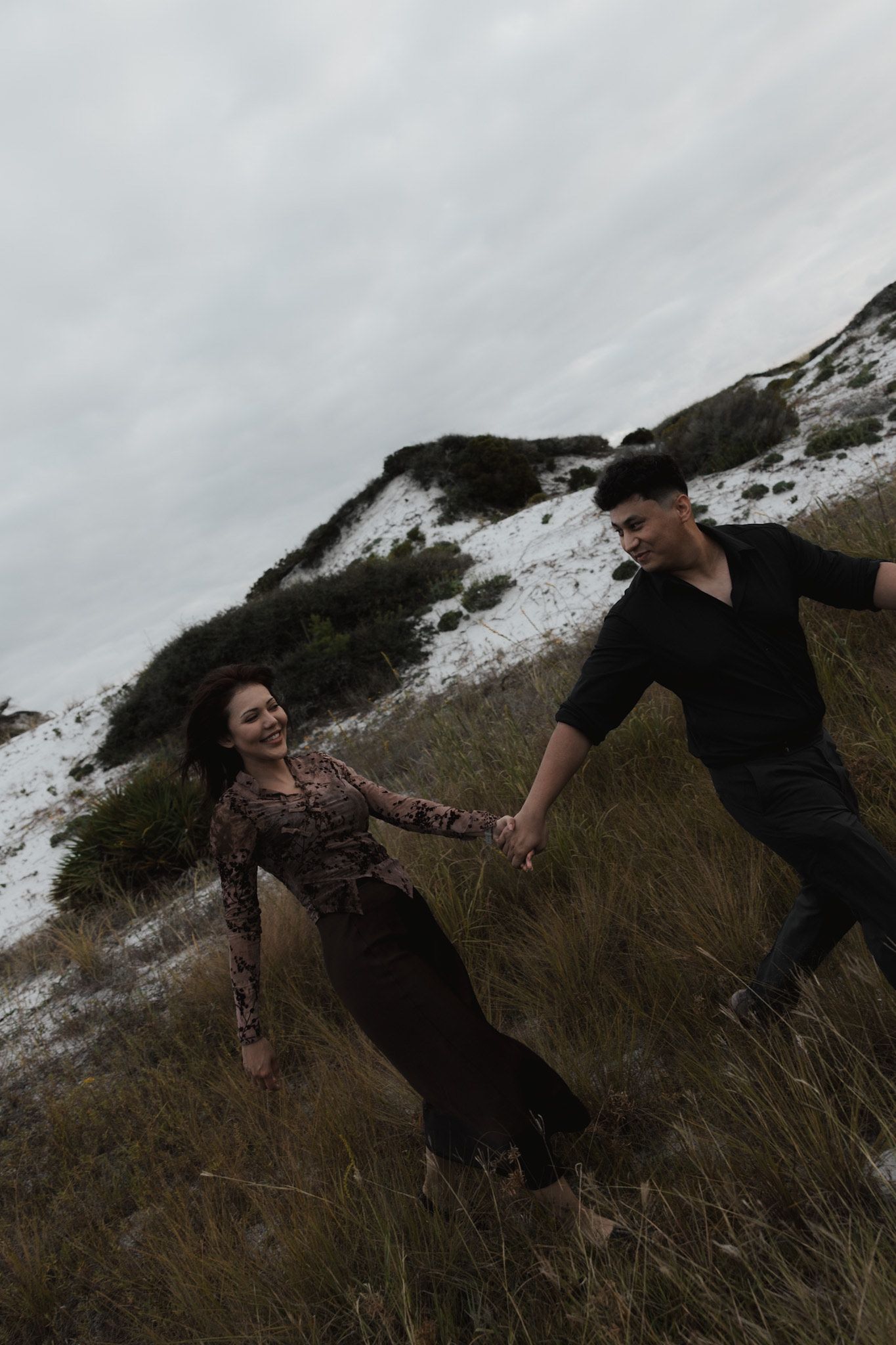 Two people playfully interact on a snowy hillside in moody lighting.