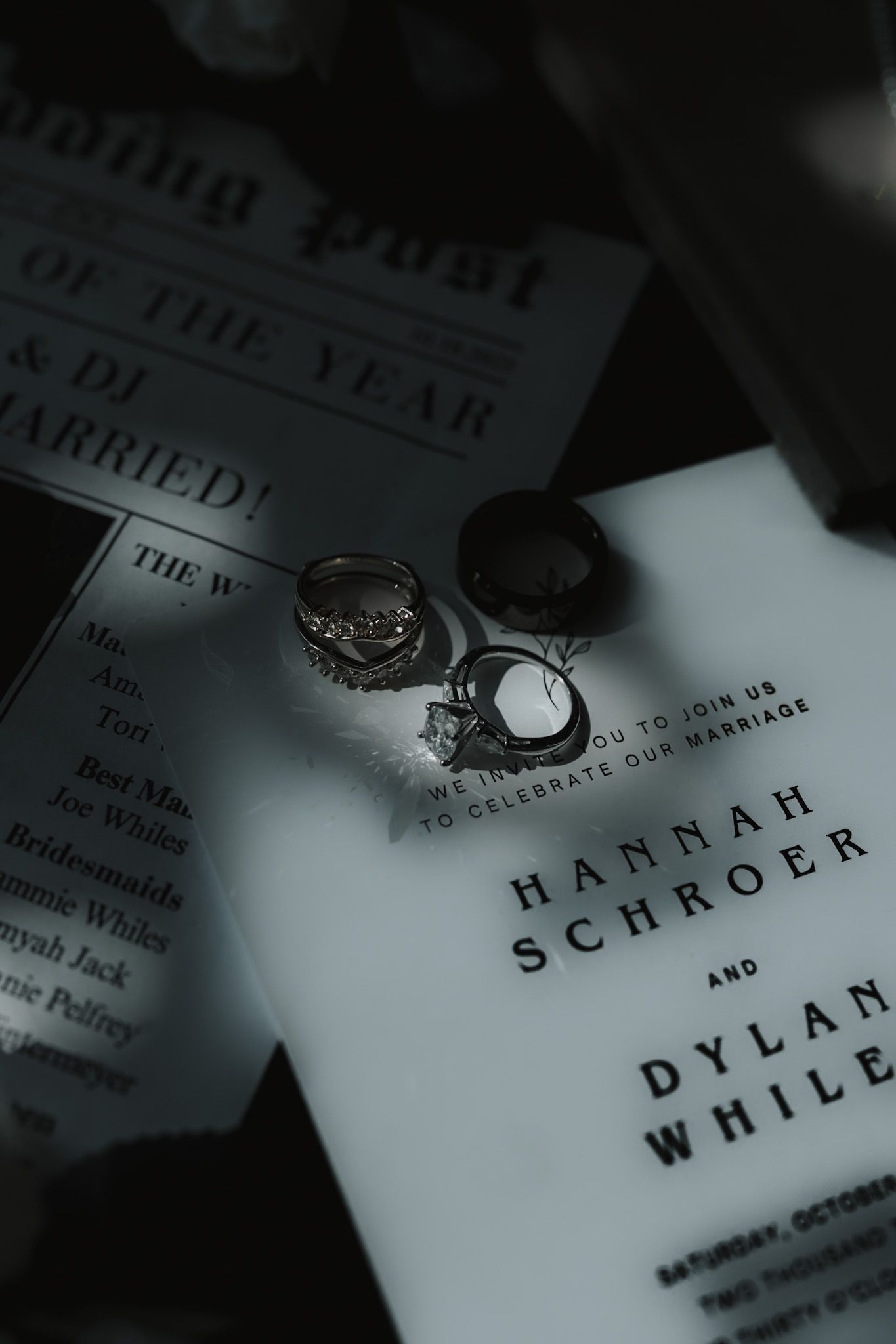 Wedding rings and invitation details in dramatic black and white lighting.