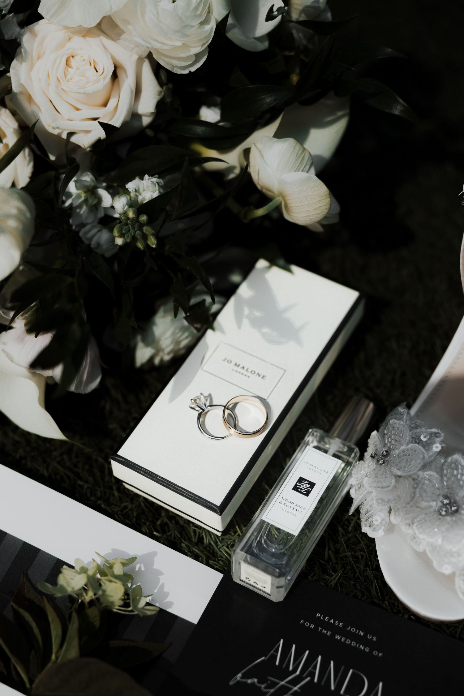 Wedding details featuring white roses, rings, and invitations on dark background.