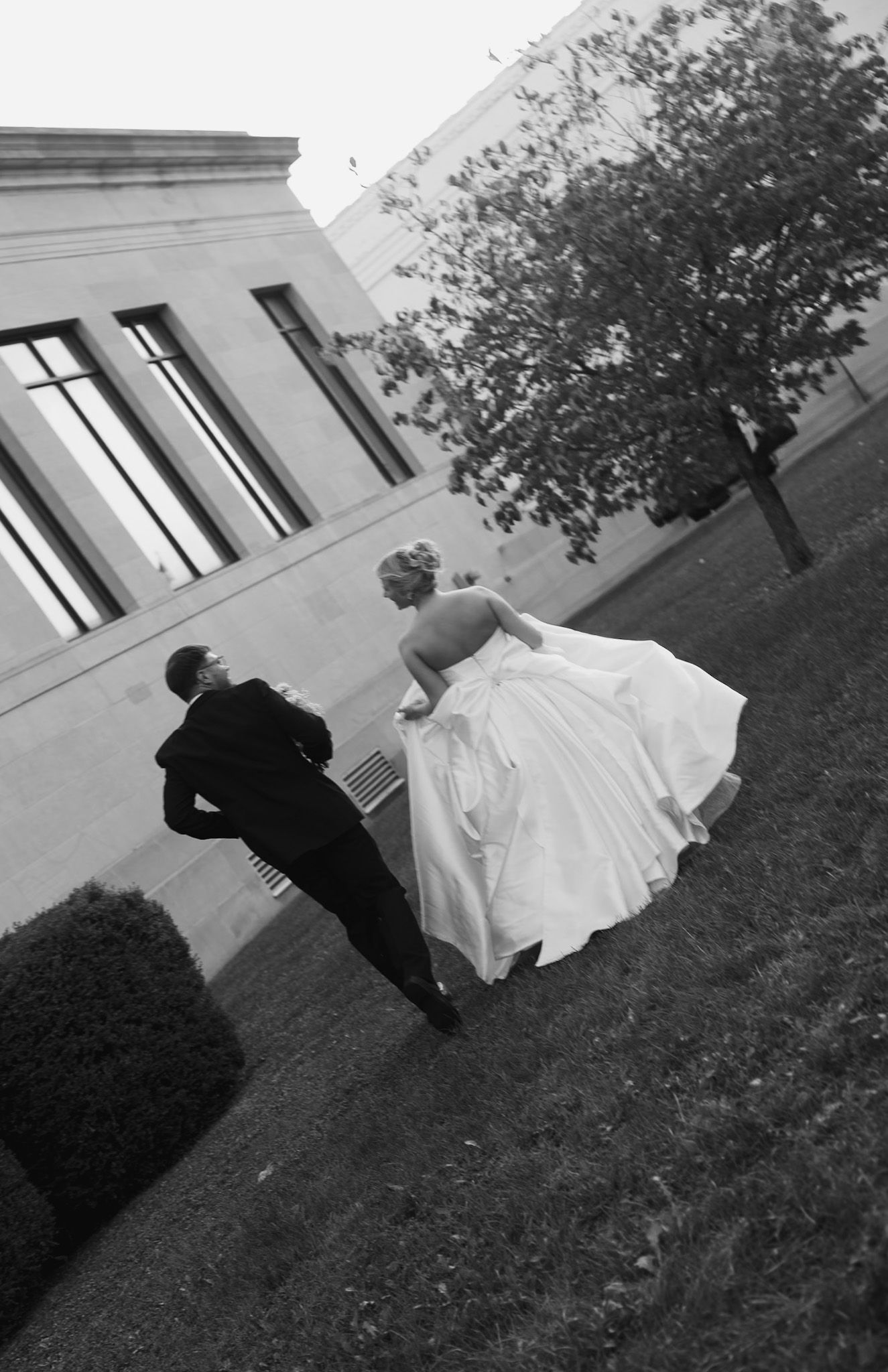 Black and white sequence showing a couple dancing playfully on grass near a building.