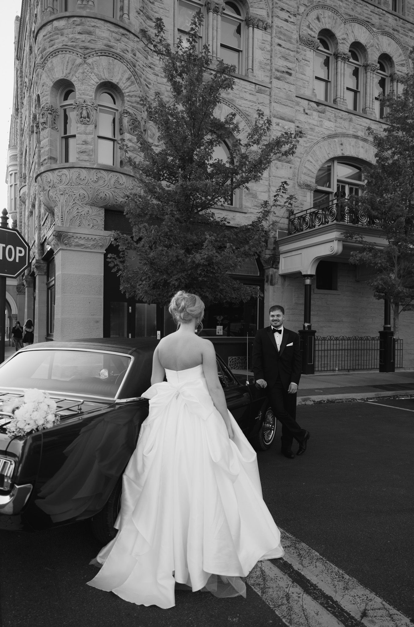 Bride in flowing white gown walking through urban street setting.