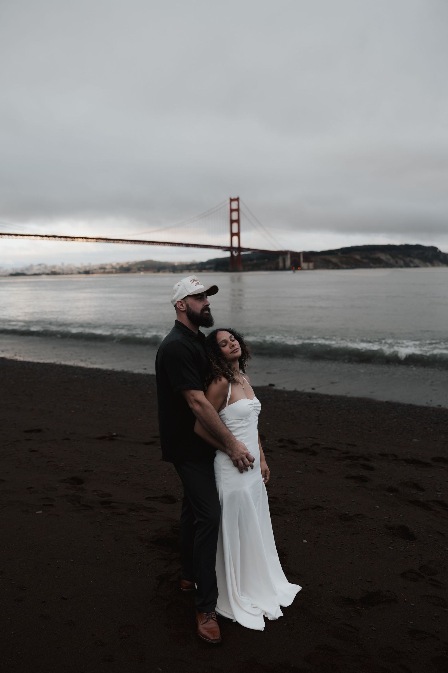Couple embracing on dark beach with iconic Golden Gate Bridge in the background.