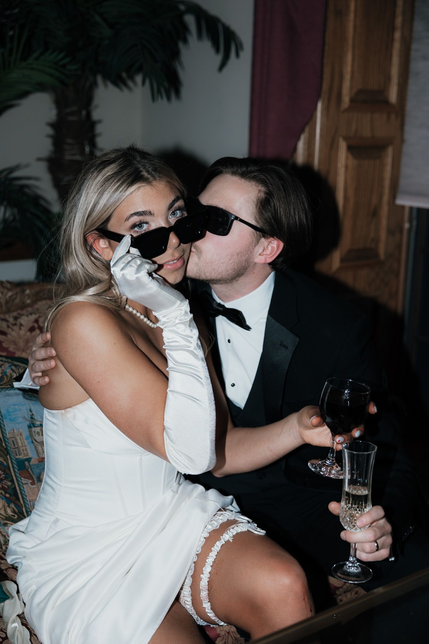 Newlyweds in white dress and tuxedo sharing a romantic moment with champagne.
