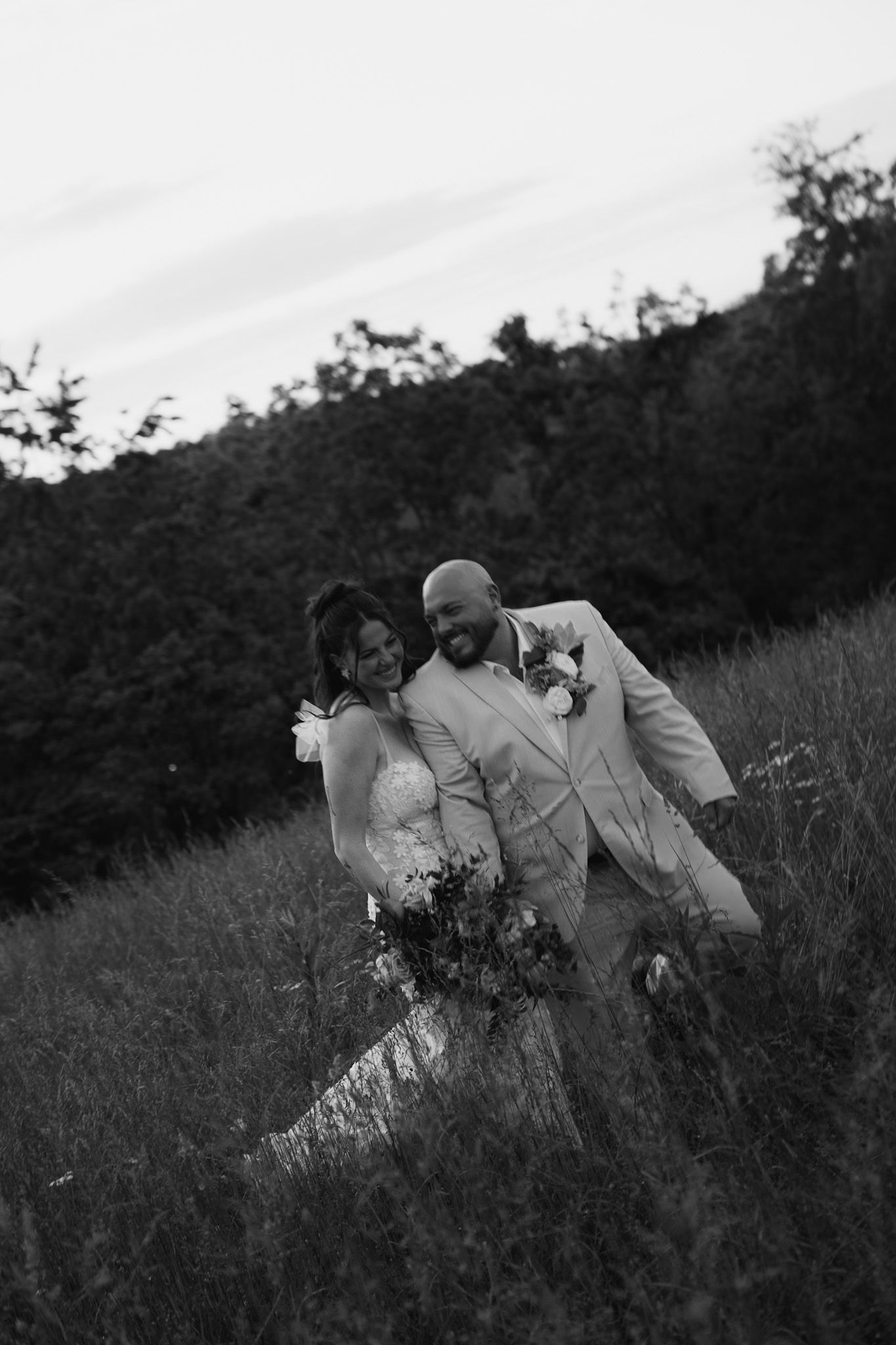 Black and white photo of couple laying in tall grass on a hillside.