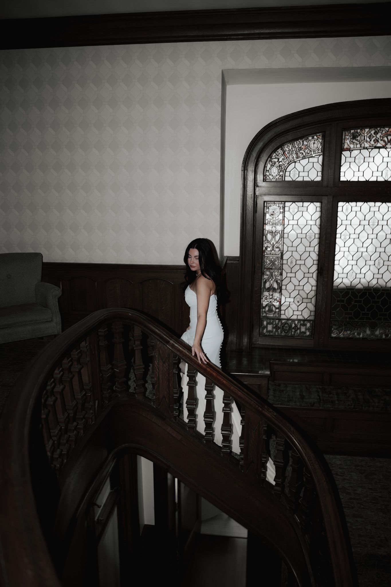 A white dress flows down ornate wooden stairs in dramatic lighting.