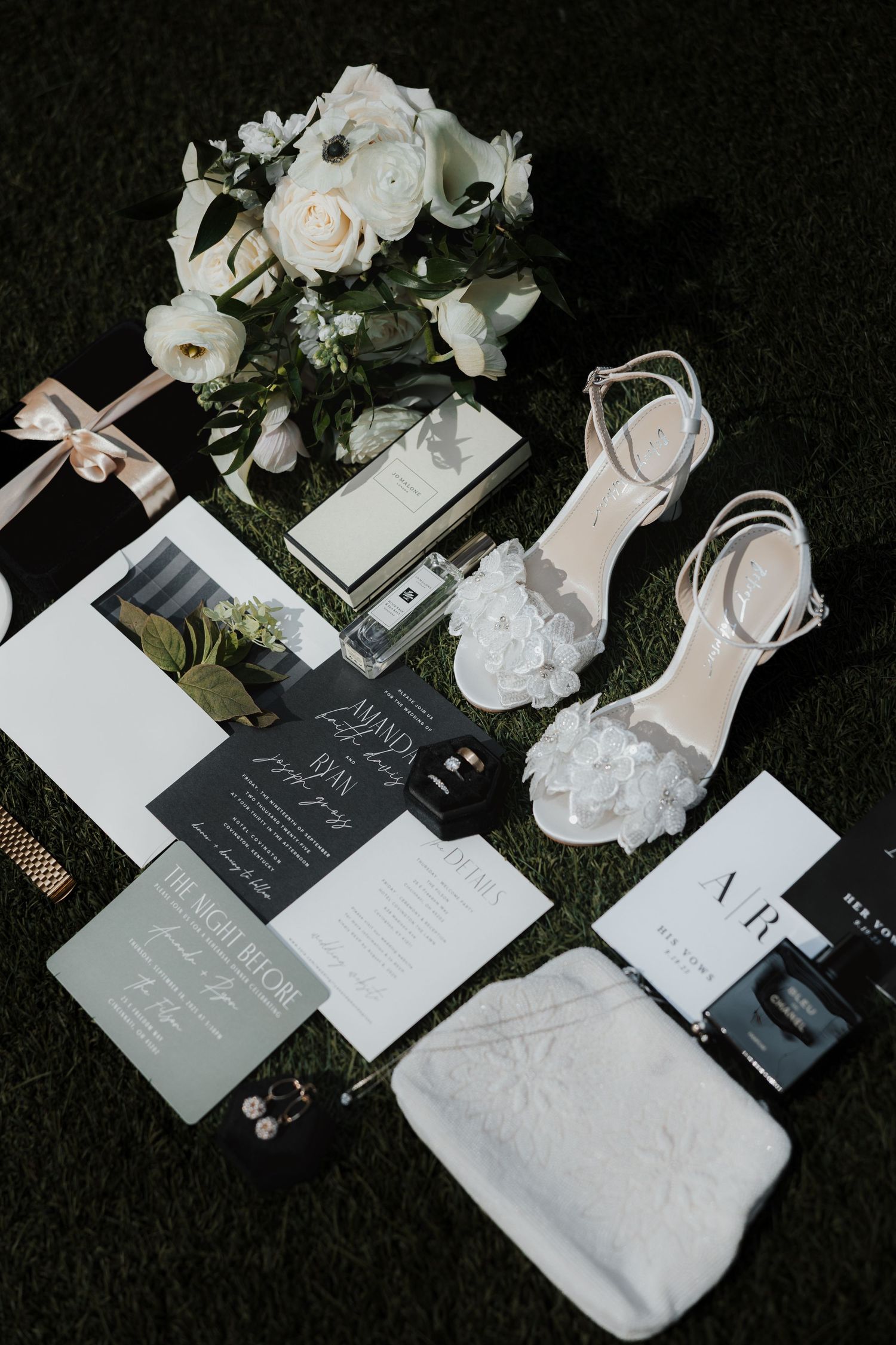 Elegant wedding flat lay with invitations, shoes, and white floral arrangements.