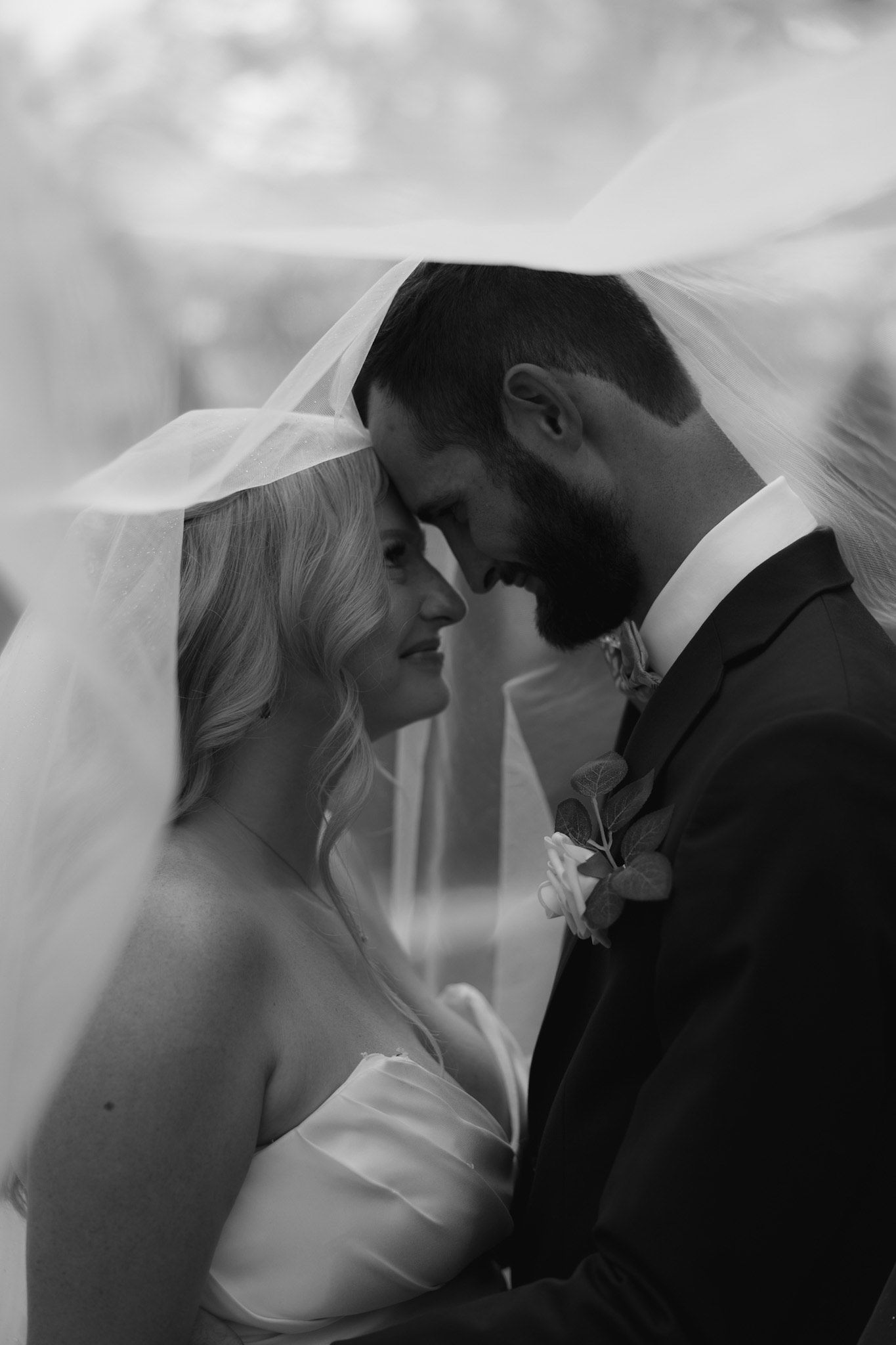 Romantic black and white portrait of newlyweds sharing an intimate moment under a veil.