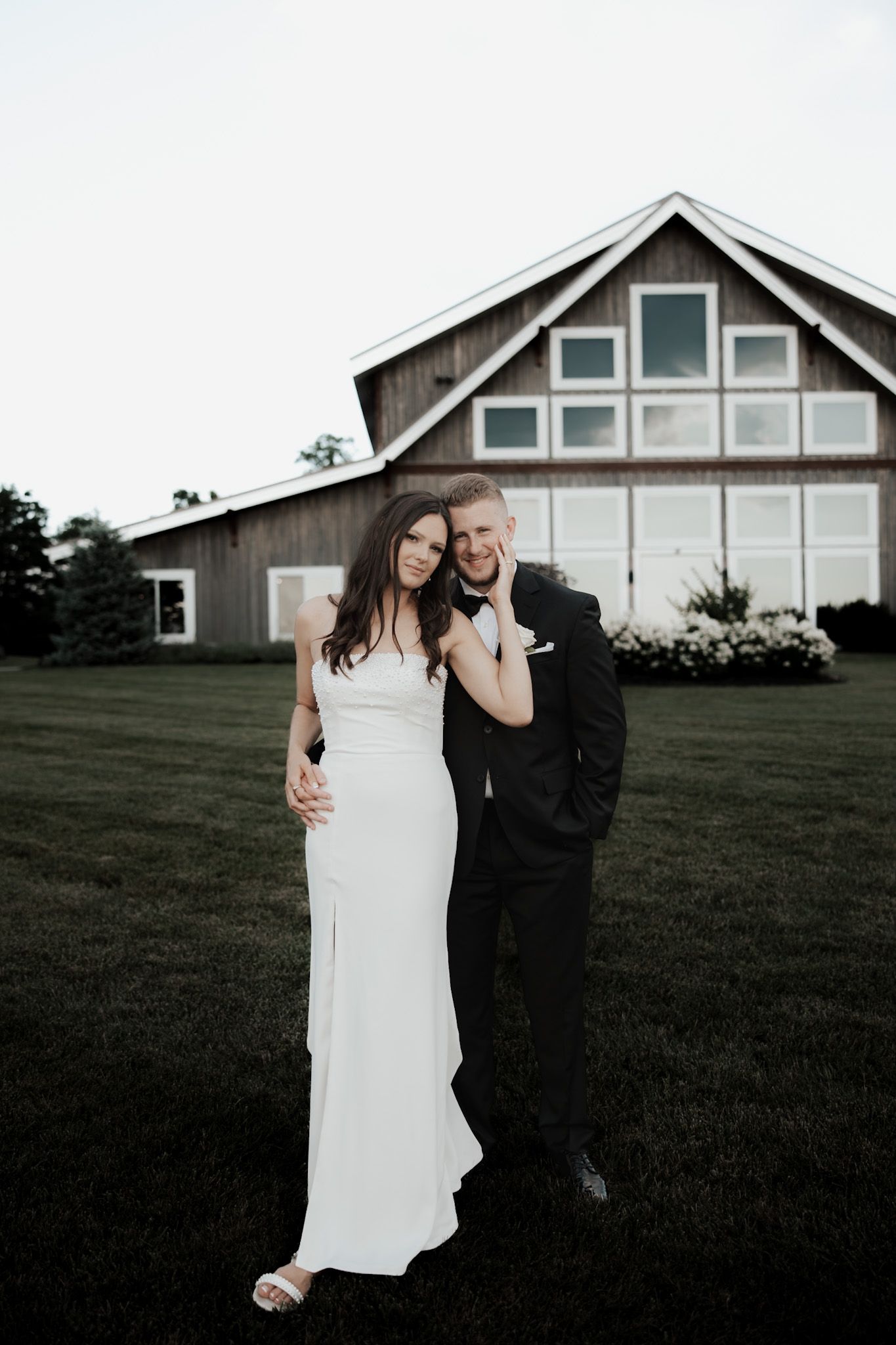 Wedding couple poses in front of a modern farmhouse with white siding.