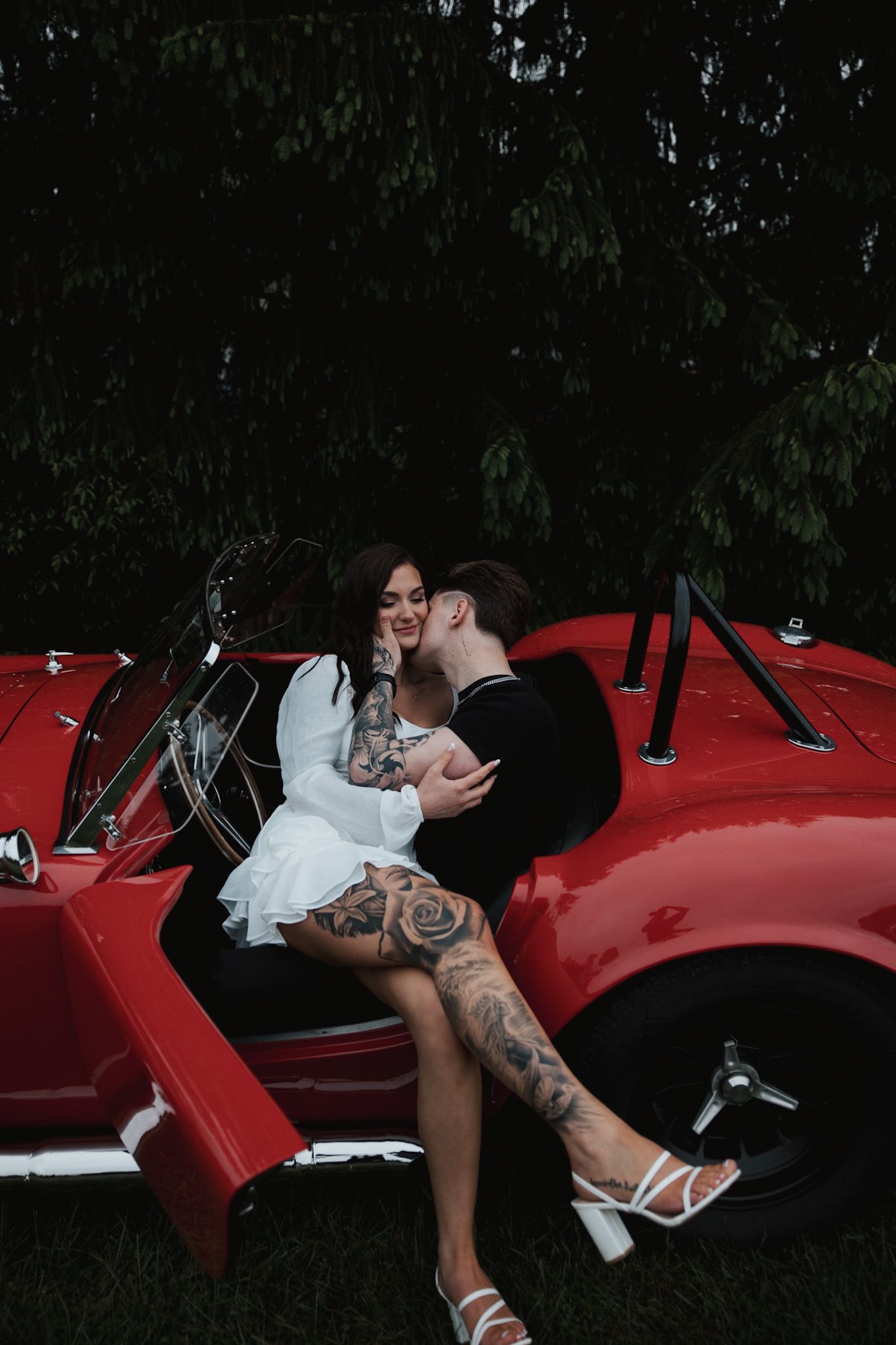 Wedding couple poses romantically against a bright red vintage car.