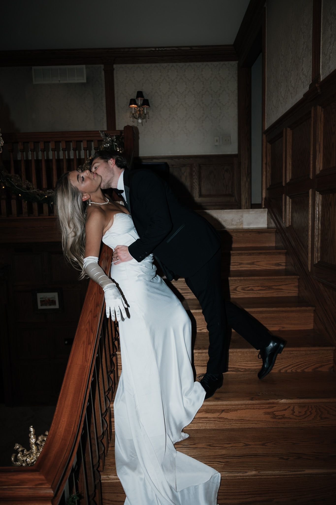 Romantic wedding couple posing on wooden staircase in dramatic lighting.