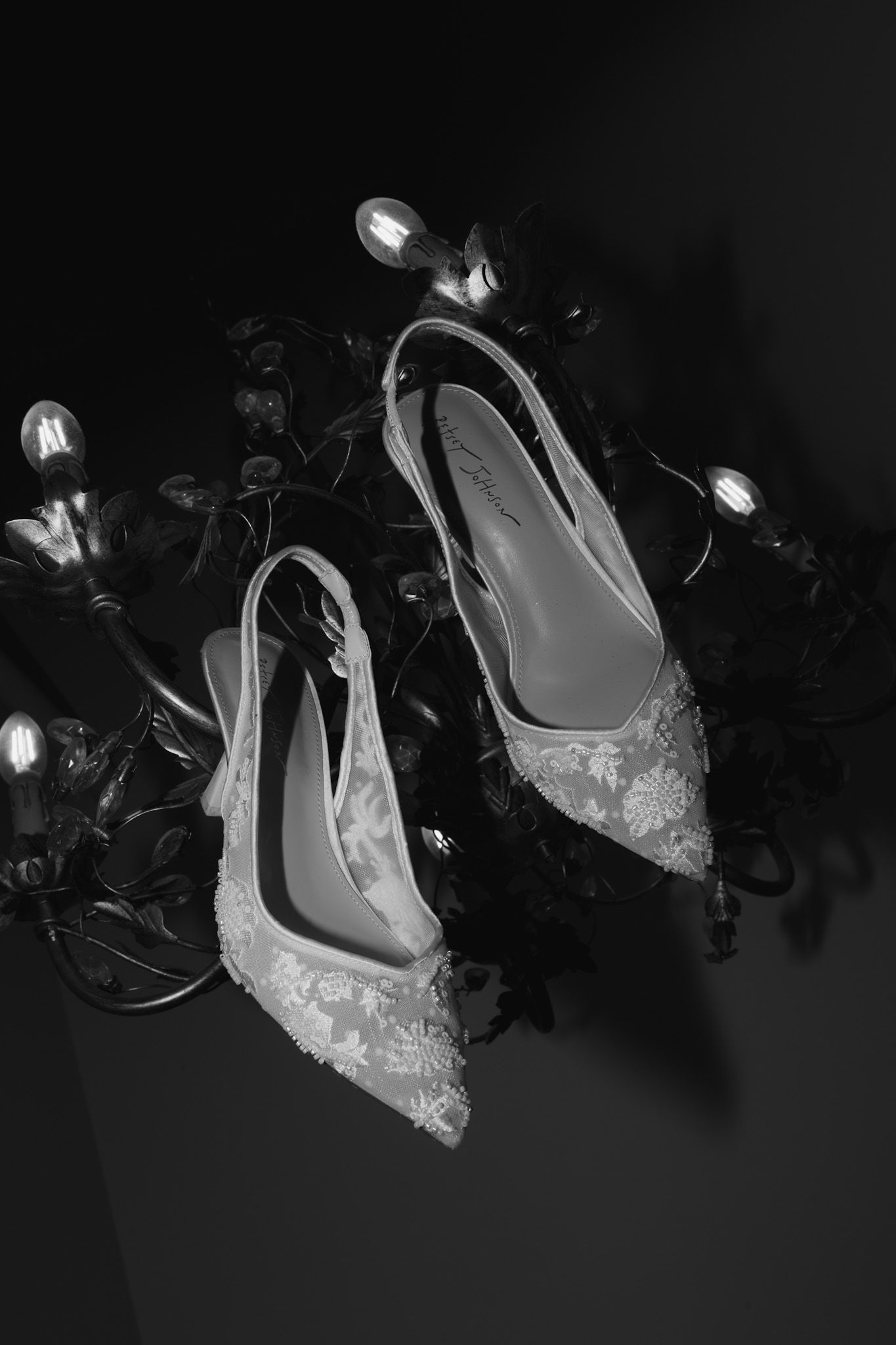 Elegant bridal shoes with lace details photographed in dramatic lighting.