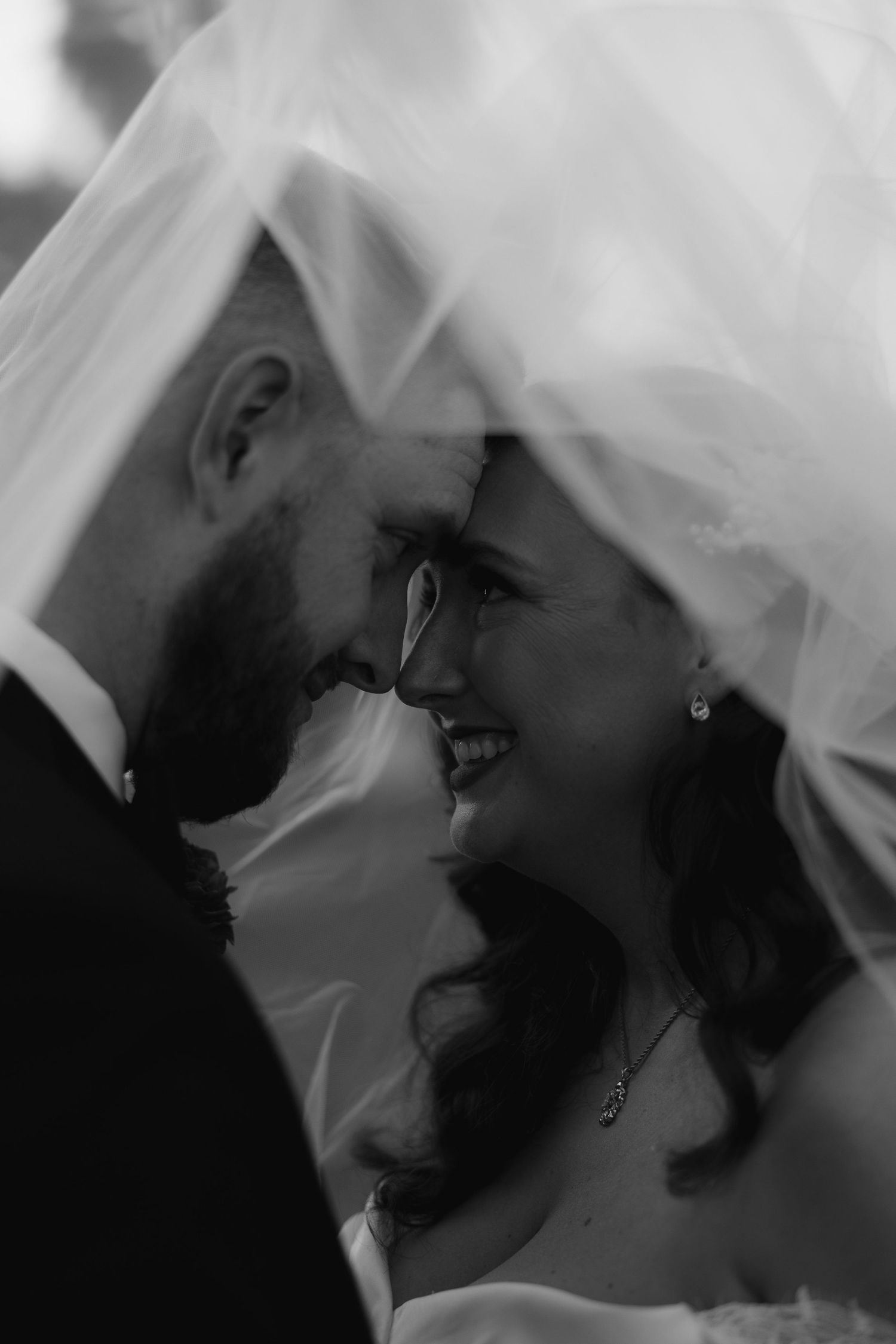A romantic moment captured through a flowing white veil in black and white.