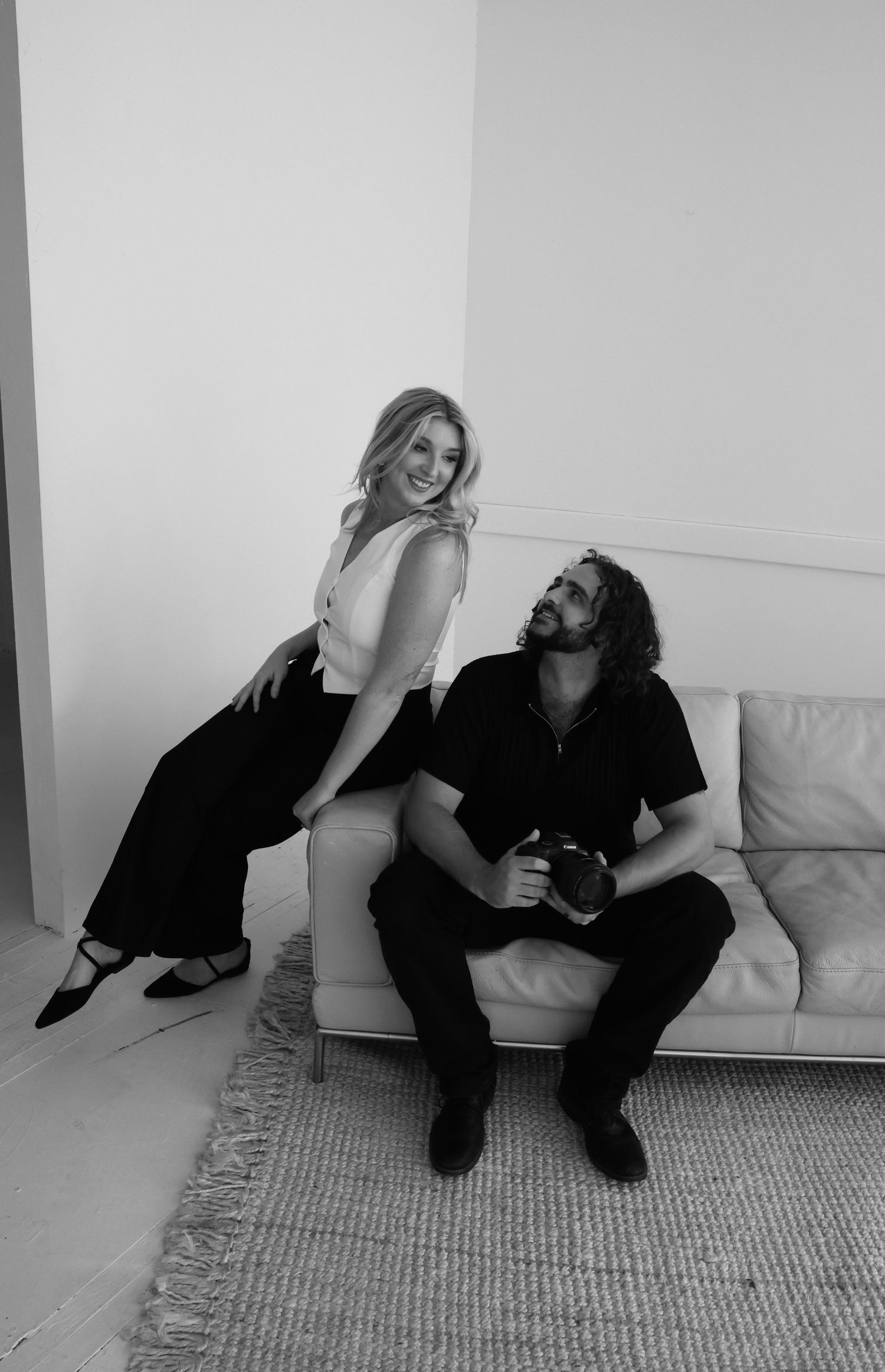 Casual couple sharing a playful moment on a white sofa in monochrome photography.