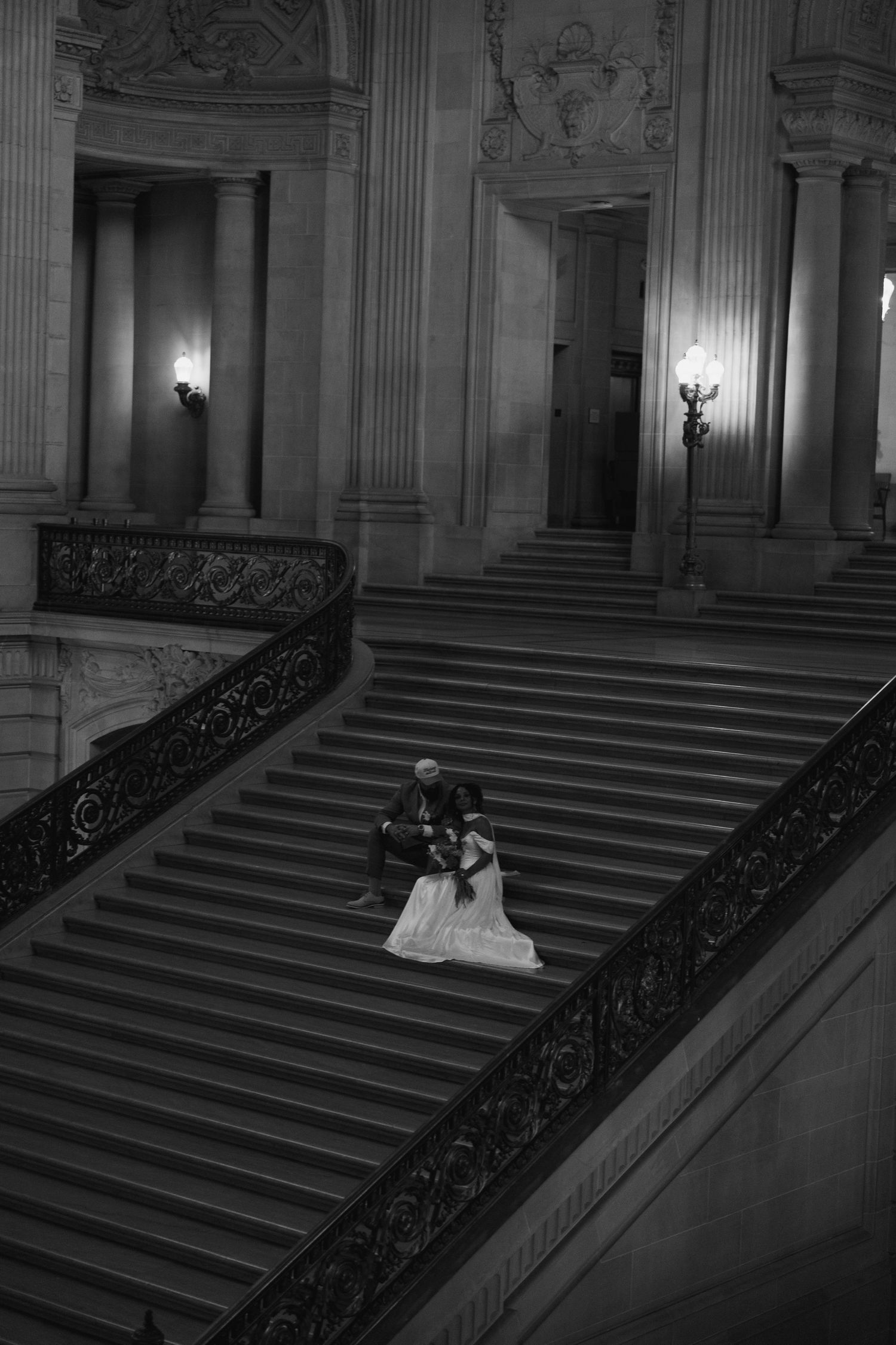 Grand staircase wedding photo in an ornate historic building with dramatic lighting.