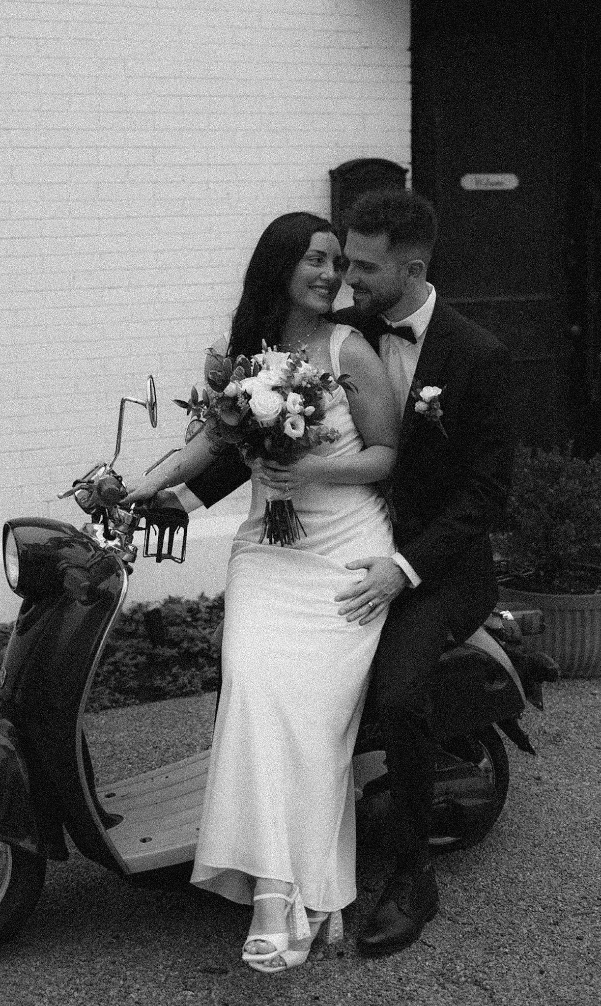 Black and white wedding photos of couple embracing on garden path with flowers.