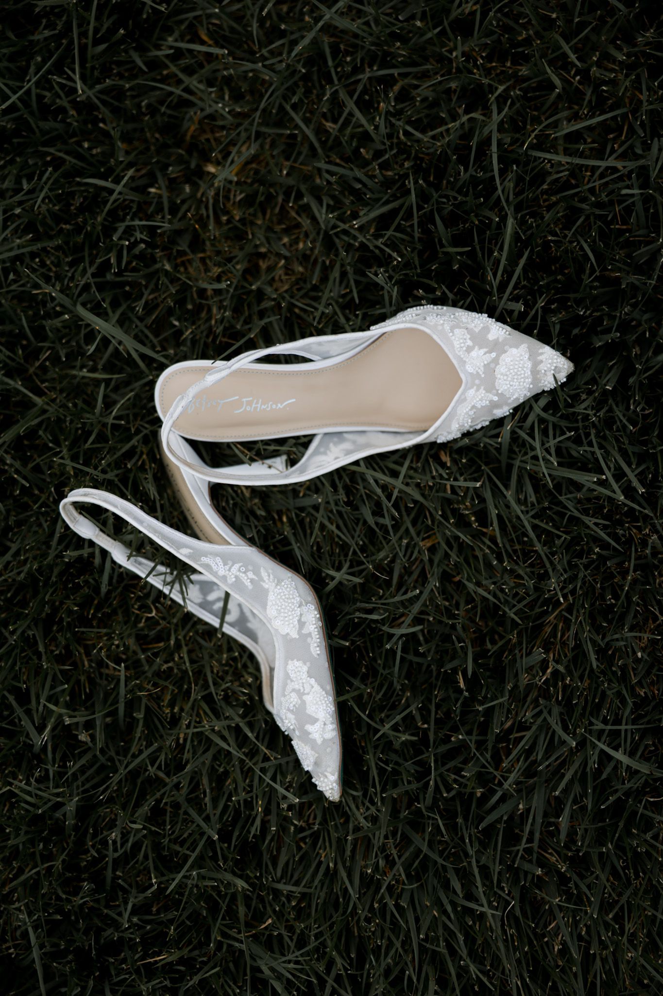 White lace wedding shoes lay scattered on dark grass.