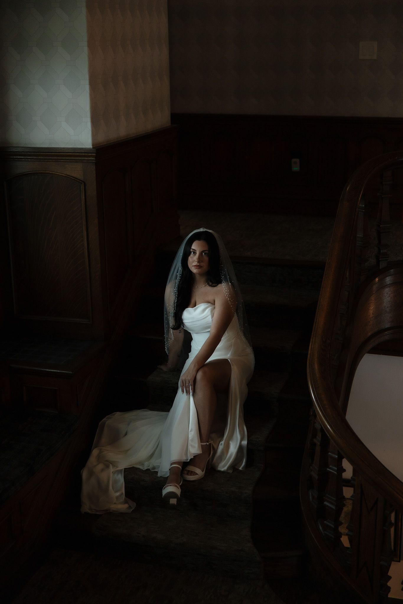 Moody bridal portrait in dark interior with dramatic window lighting.