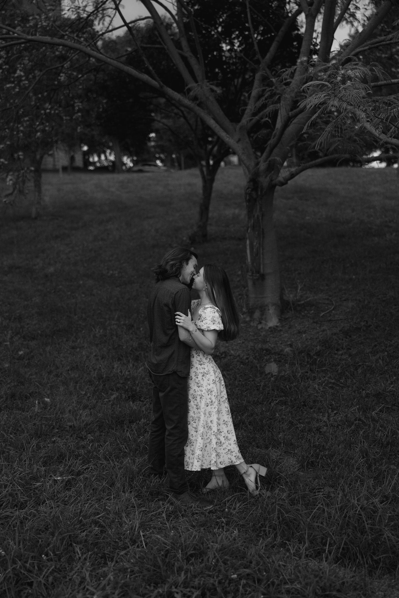 A black and white photo of someone in a dress twirling in a field surrounded by trees.