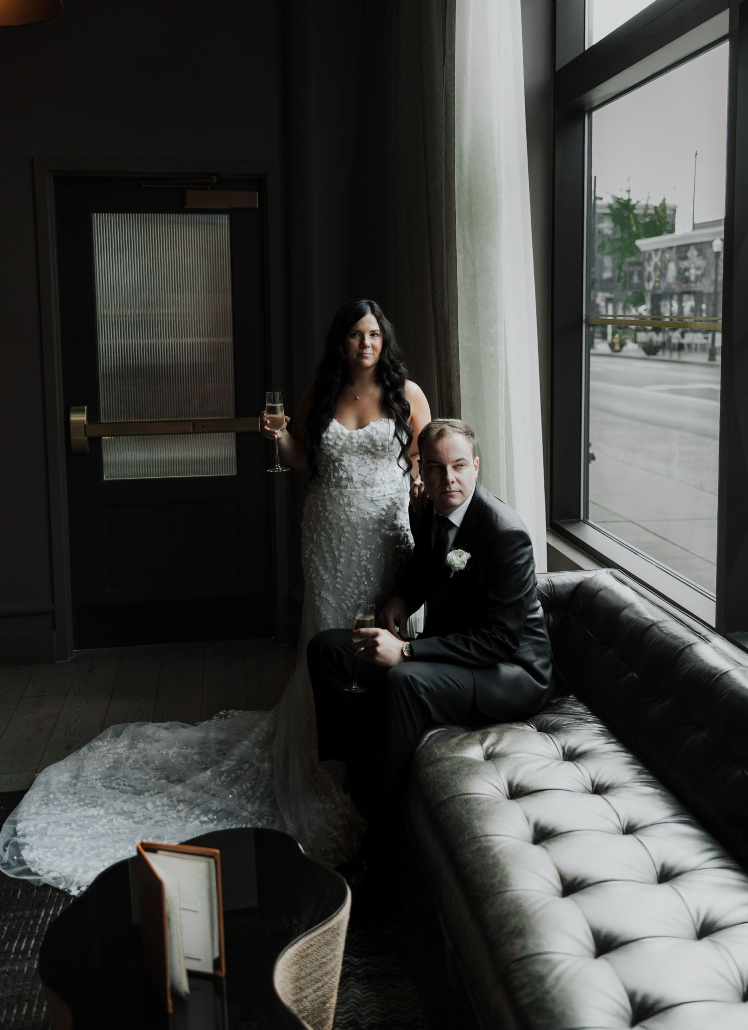 Elegant couple posing by window in modern interior with tufted leather couch.