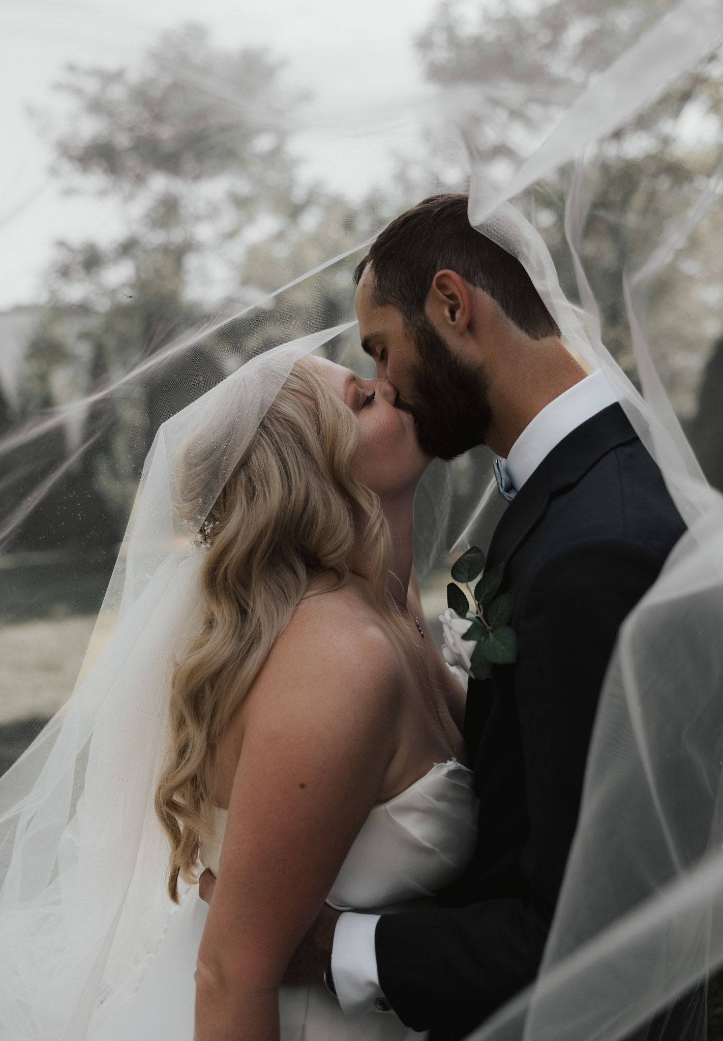 Tender moment between newlyweds captured under flowing veil with soft natural lighting.