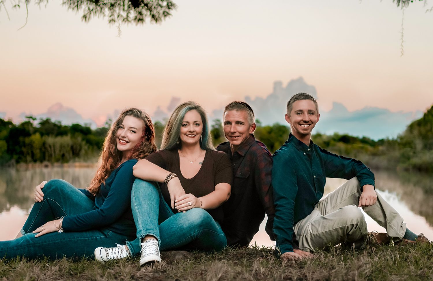 A group of people in matching dark outfits lying in the grass during a casual outdoor photo session at sunset.