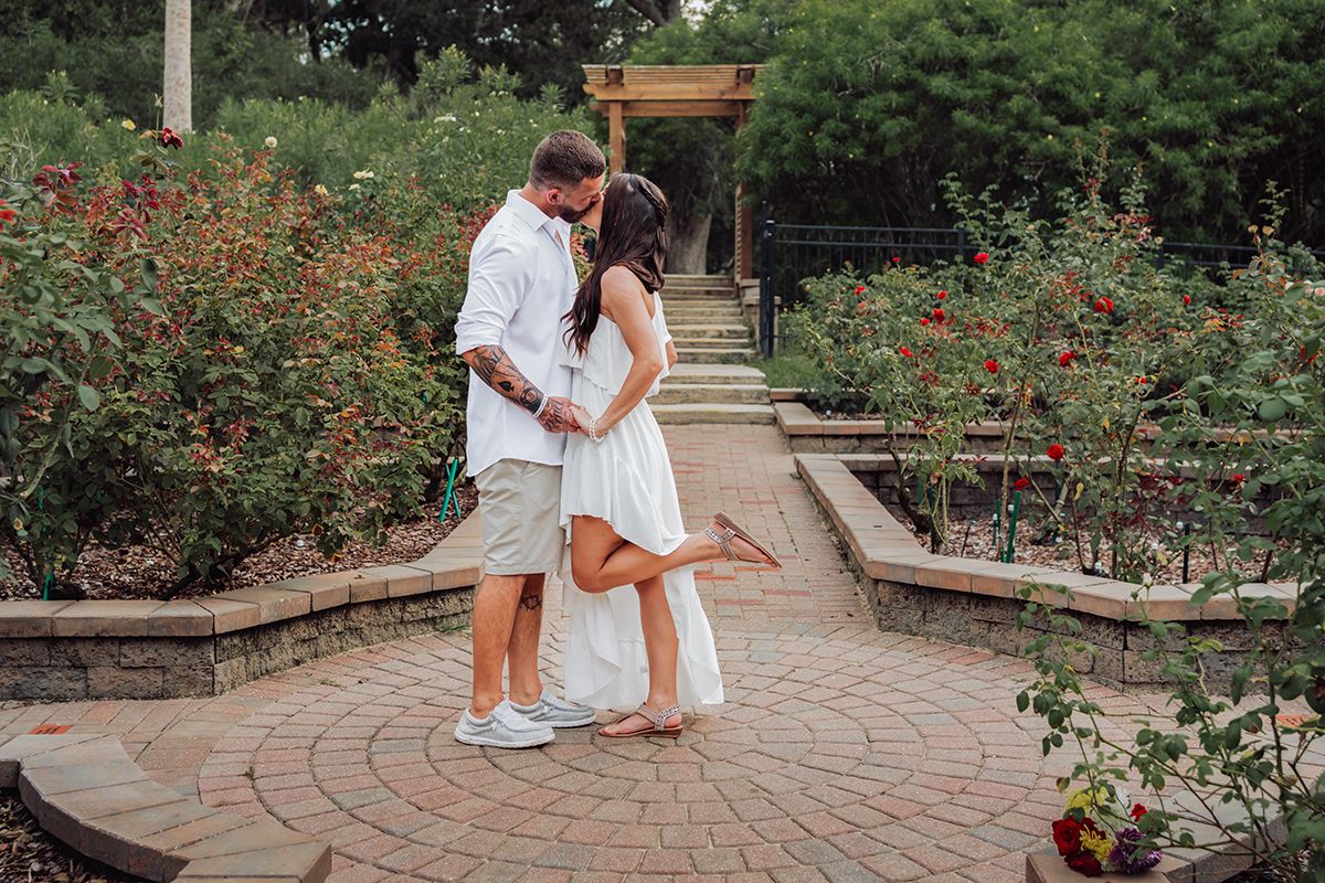 A couple shares a tender moment together in a beautiful garden setting with brick pathways and blooming flowers.
