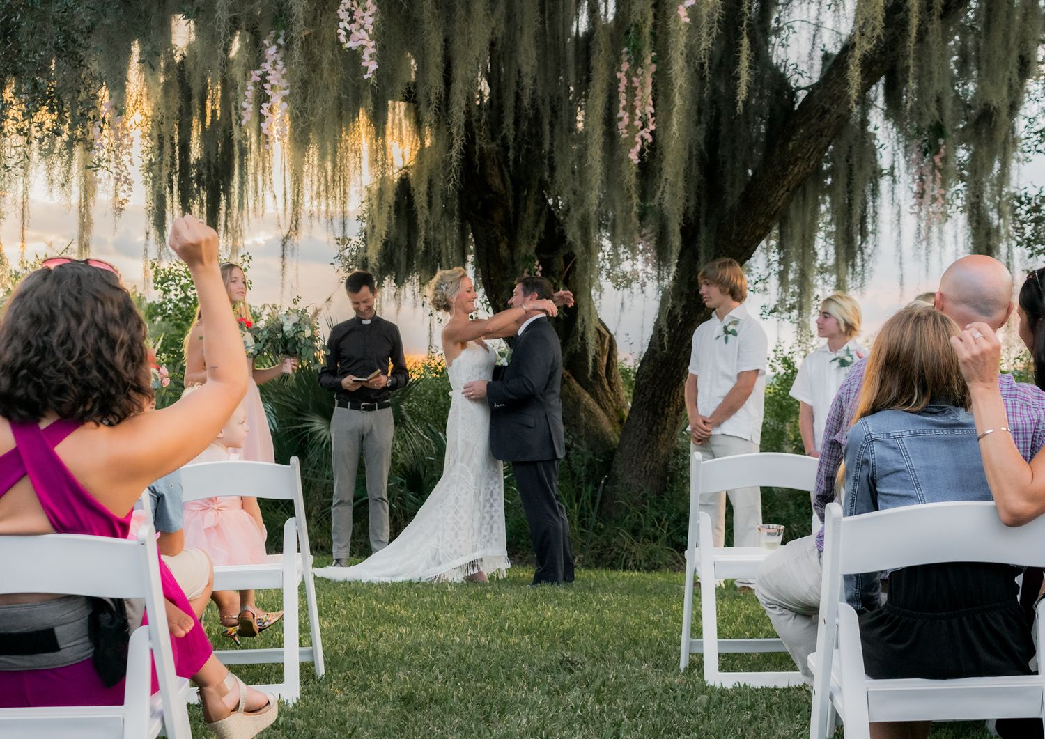 A series of outdoor wedding ceremony photos showing guests seated in white chairs under moss-draped trees at sunset.