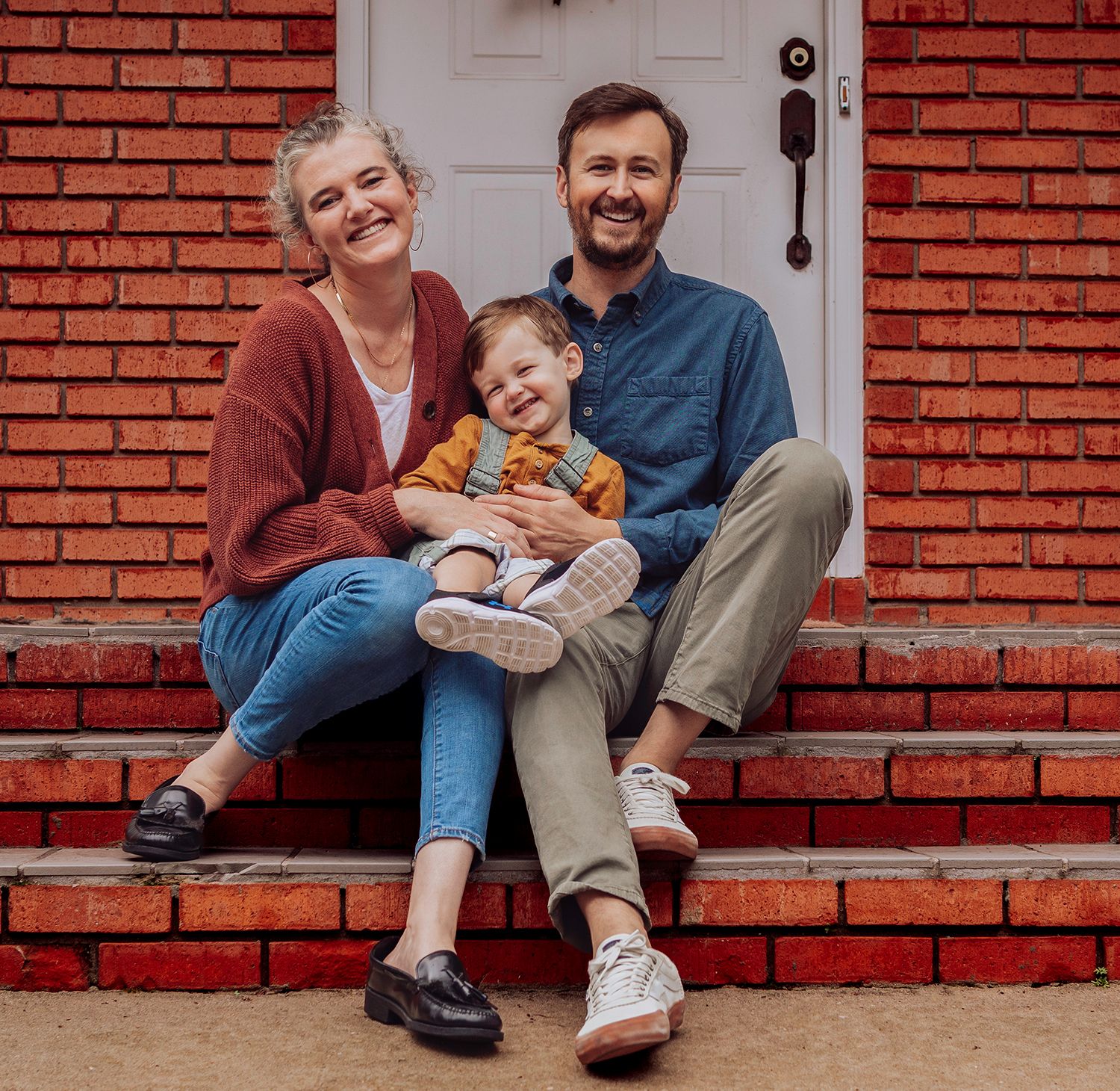 Family sitting together on red brick steps in front of white door, wearing casual clothing and smiling family photos in Gainesville Florida